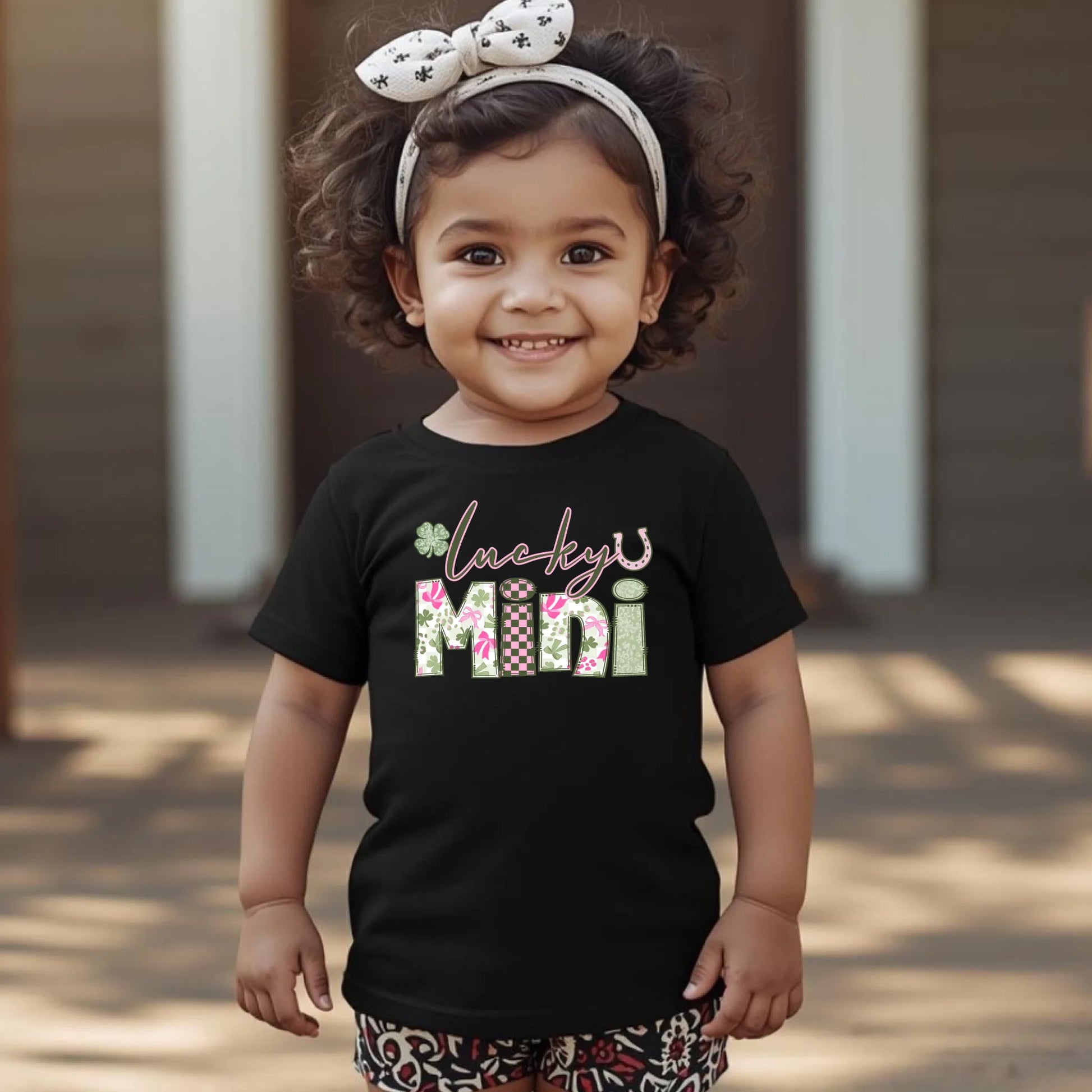 Child wearing a black t-shirt with 'Lucky Mini' text and floral design outdoors.