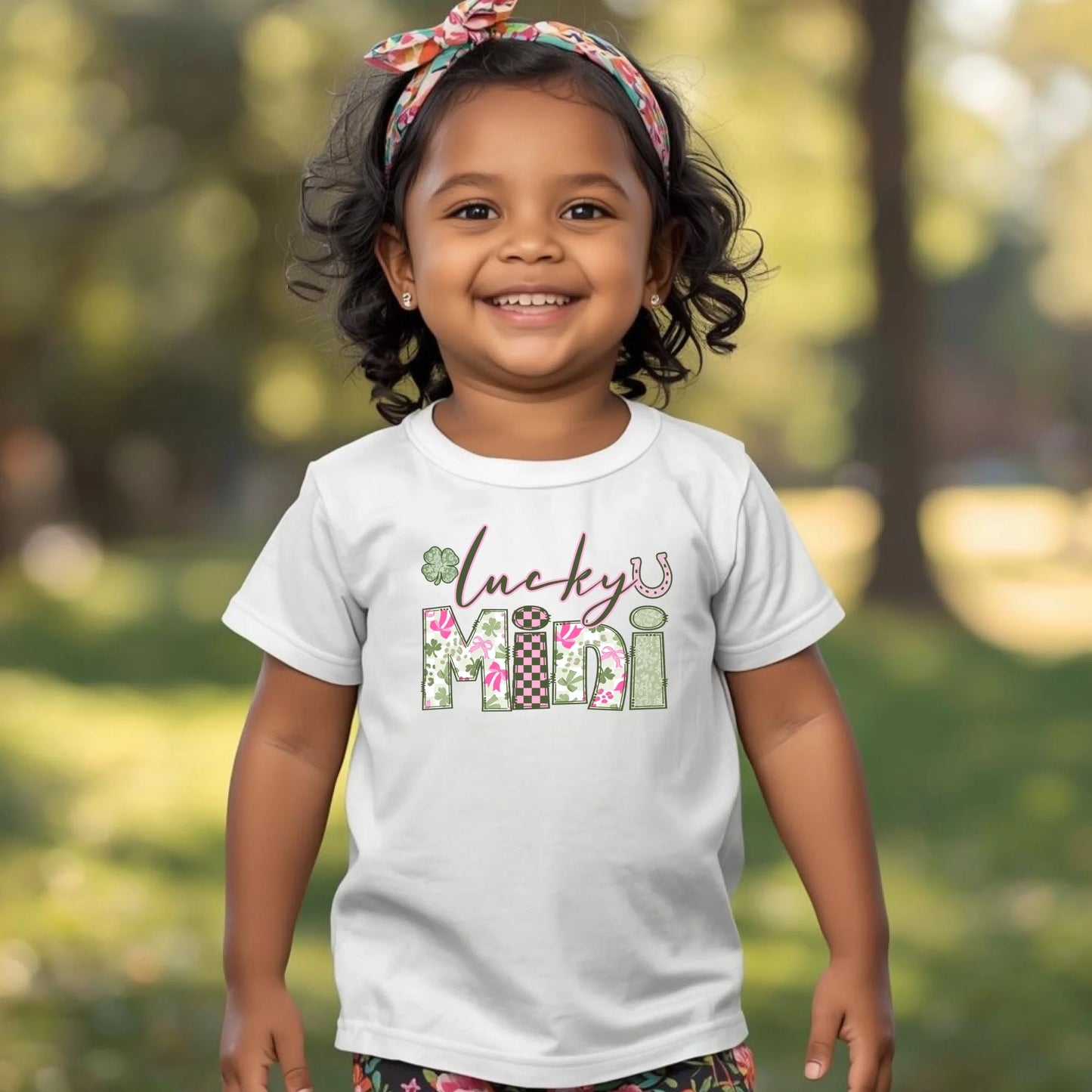 Child wearing a white t-shirt with 'lucky mini' text in a garden setting