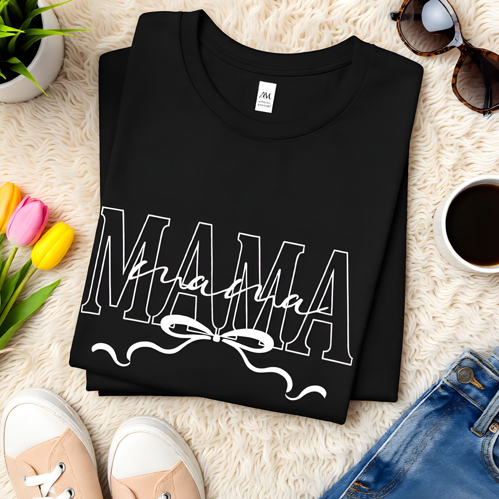 Folded black Bella Canvas Mama t-shirt featuring a minimalist script design with bow detail on a neutral flat lay background.