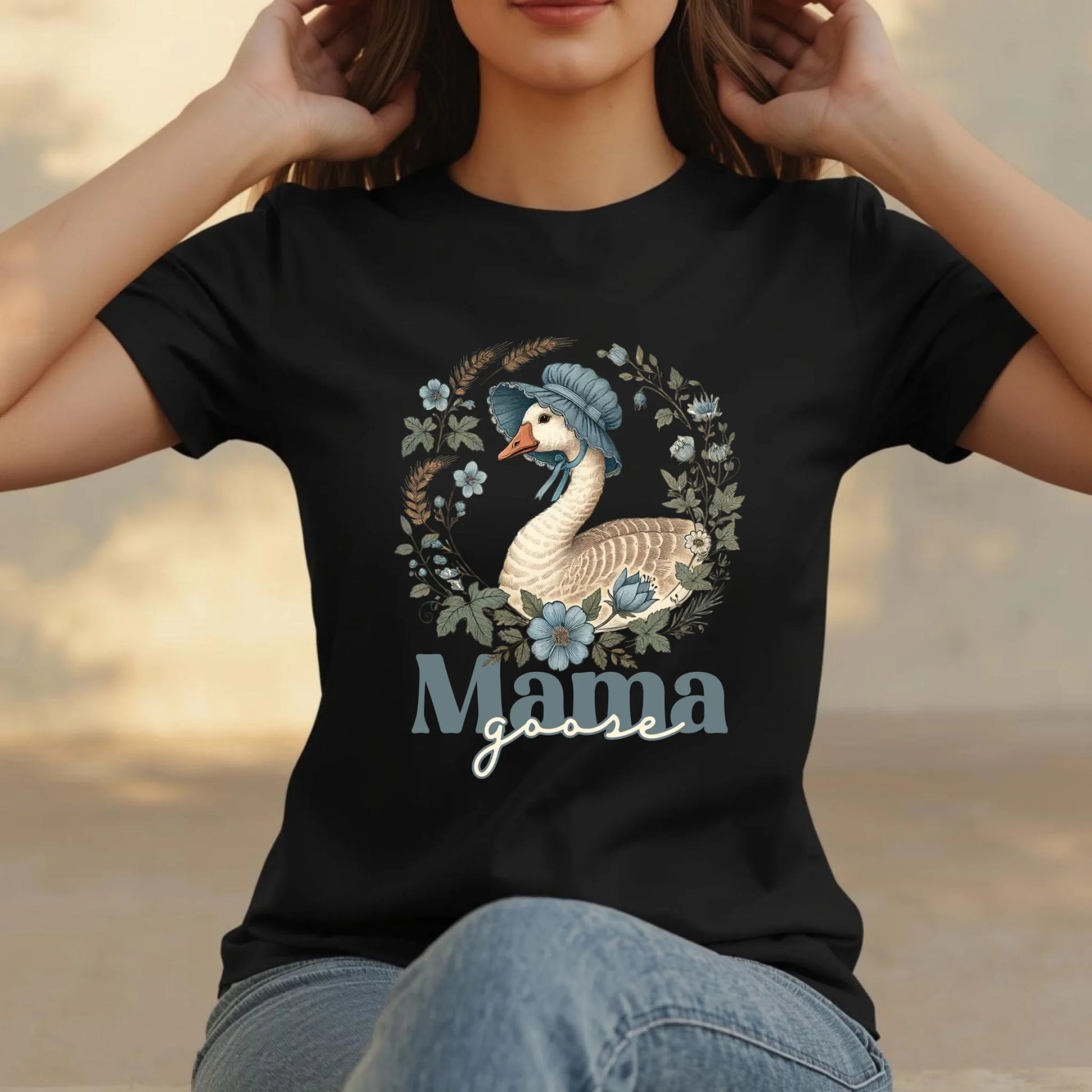 Close-up lifestyle shot of a woman wearing a black Mama Goose floral graphic t-shirt with a wreath-style goose illustration and soft botanical details.