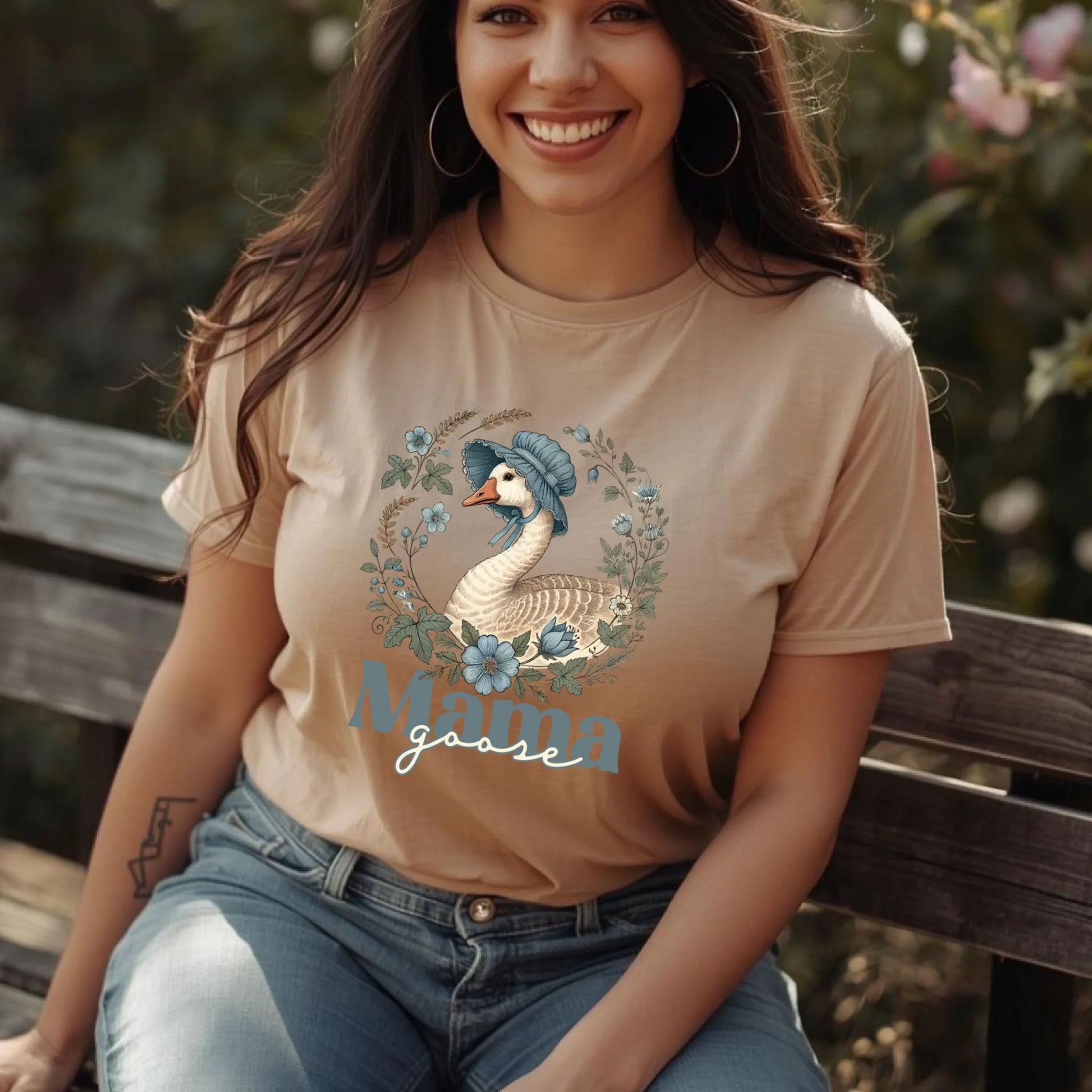 Woman wearing a neutral-tone Mama Goose floral t-shirt, styled casually with denim, featuring a classic goose and botanical wreath design.
