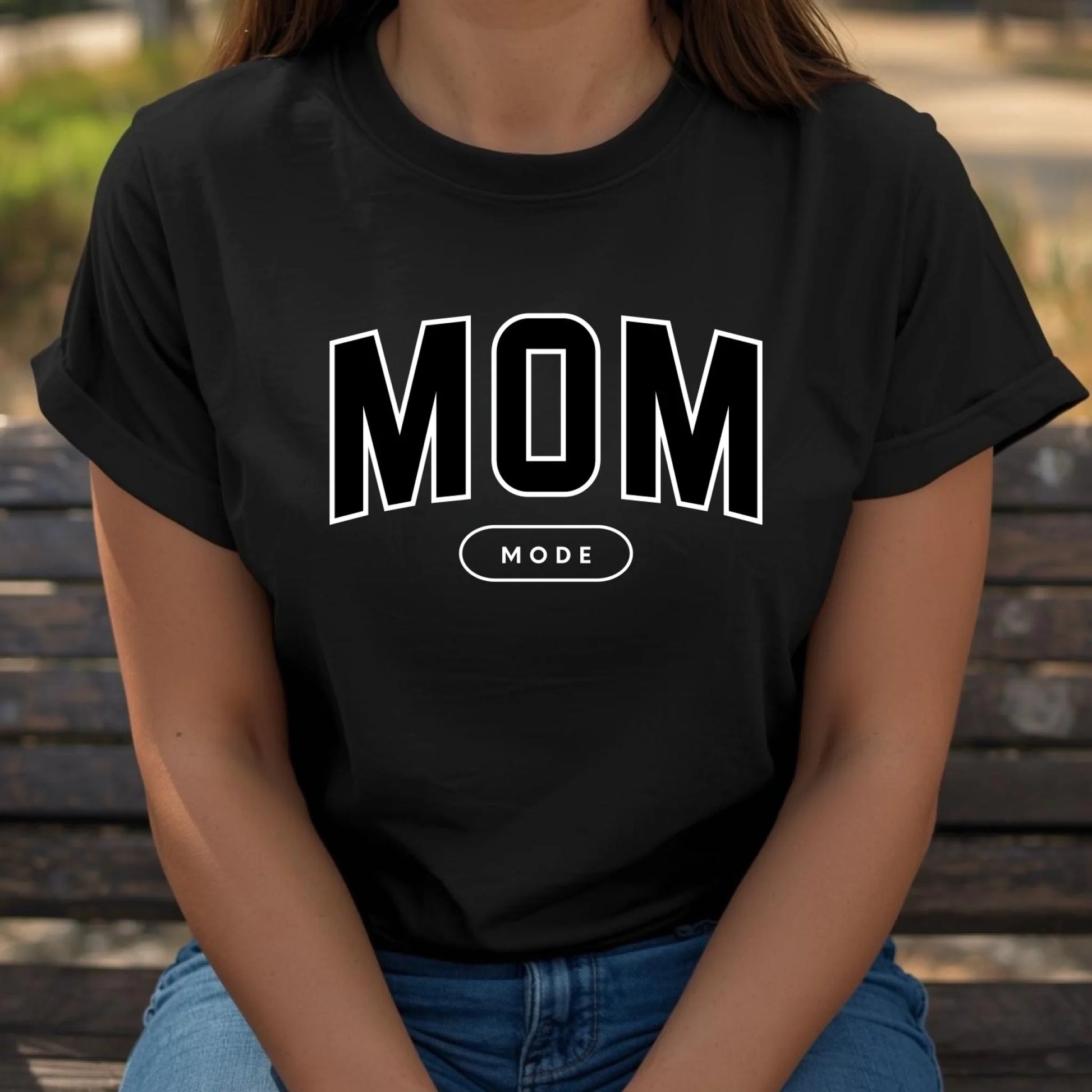 Person wearing a black t-shirt with 'MOM MODE' text sitting on a wooden bench.