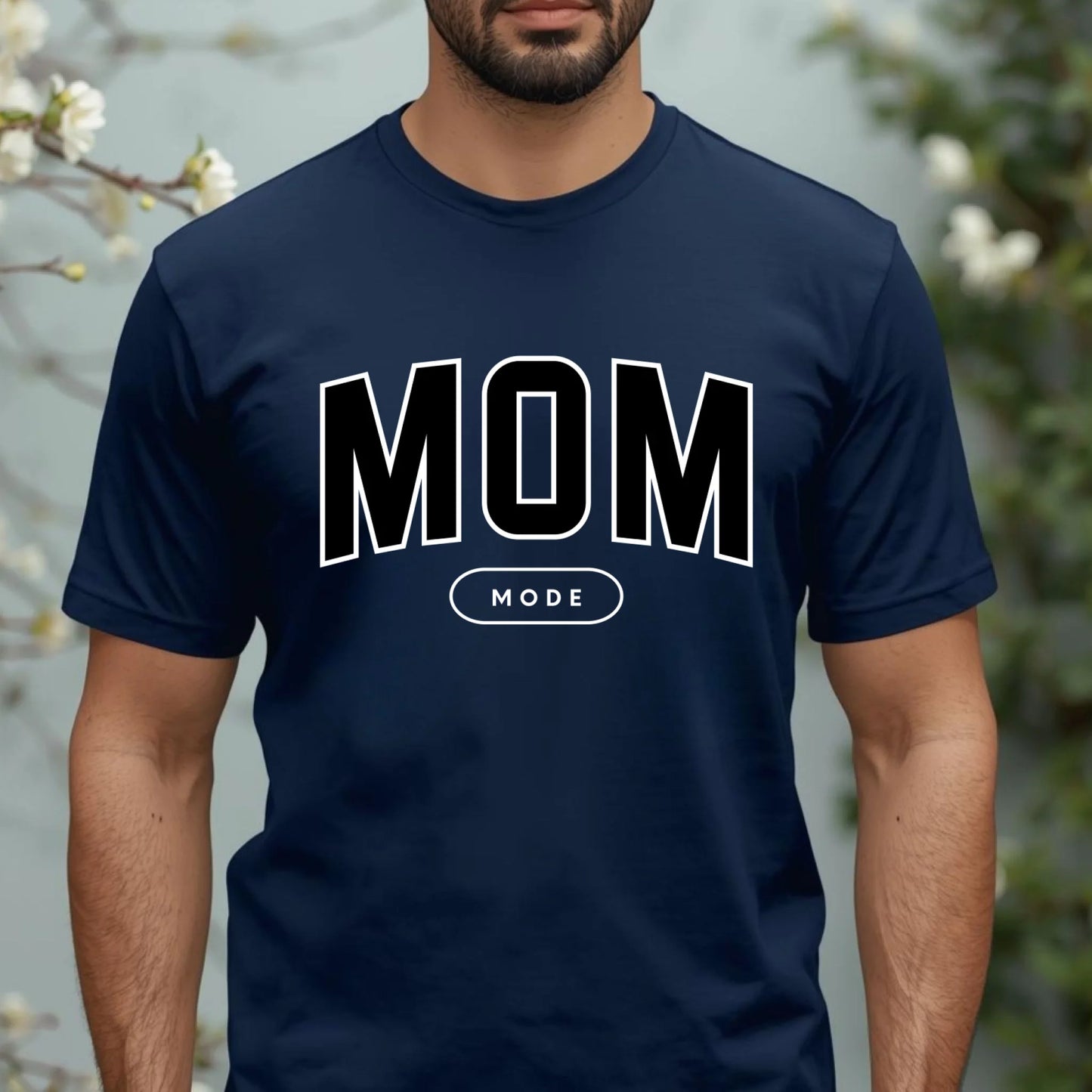 Navy blue t-shirt with 'MOM MODE' text worn by a person, against a blurred natural background.