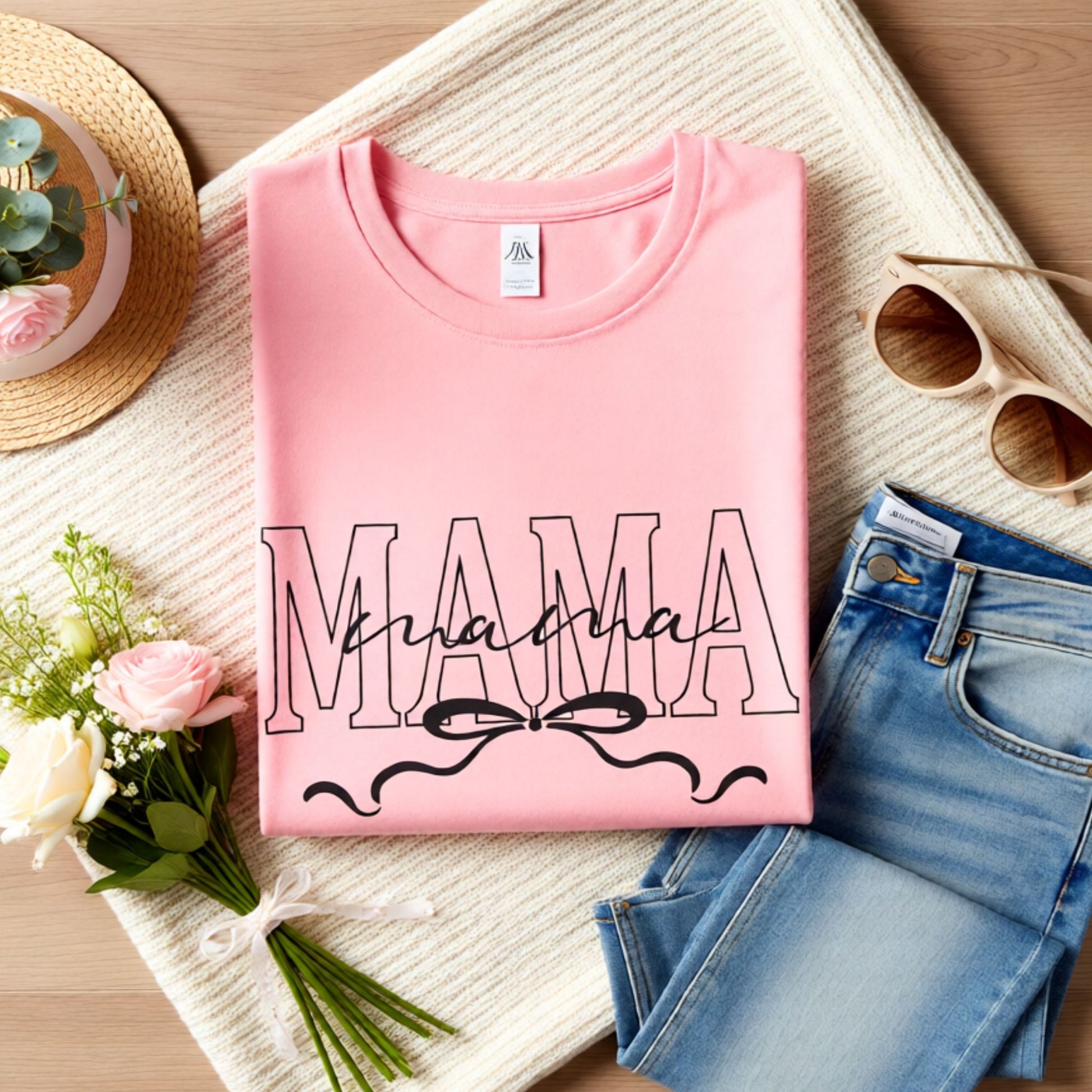 Folded pink Bella Canvas Mama t-shirt with elegant script and bow design on a soft lifestyle flat lay background.