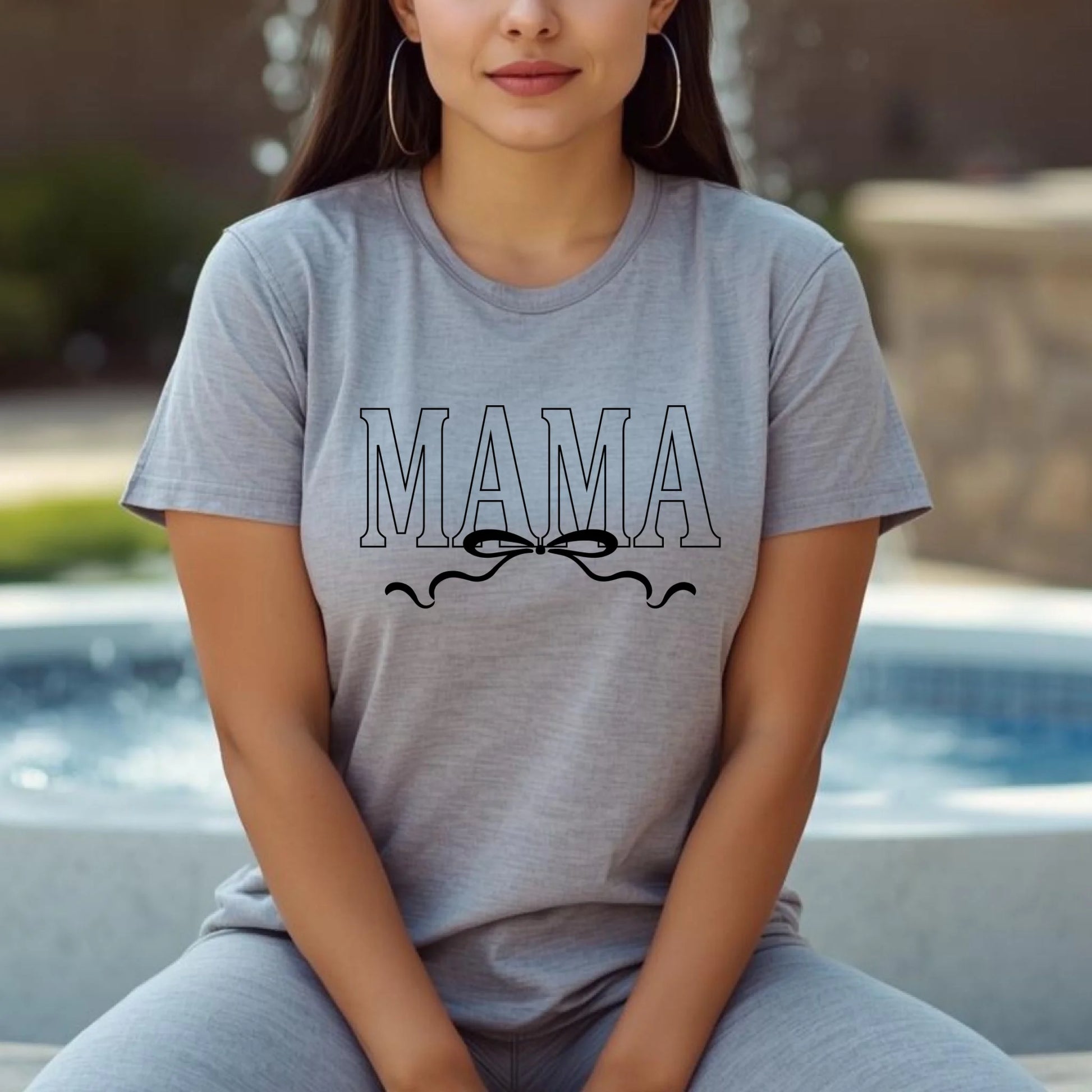 Woman wearing a gray t-shirt with 'MAMA' printed on it, sitting by a pool.