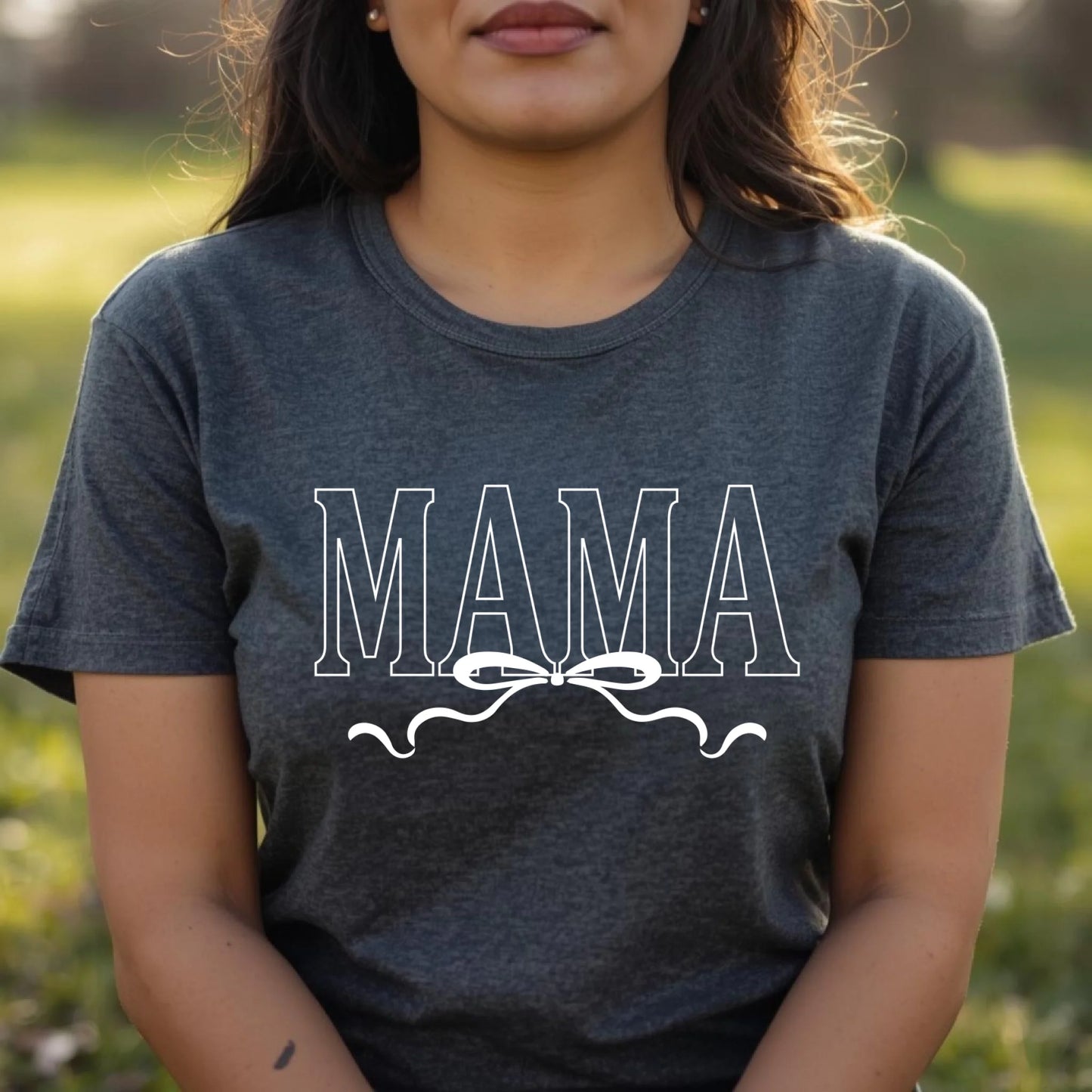 Person wearing a dark gray t-shirt with 'MAMA' printed on it, standing outdoors.
