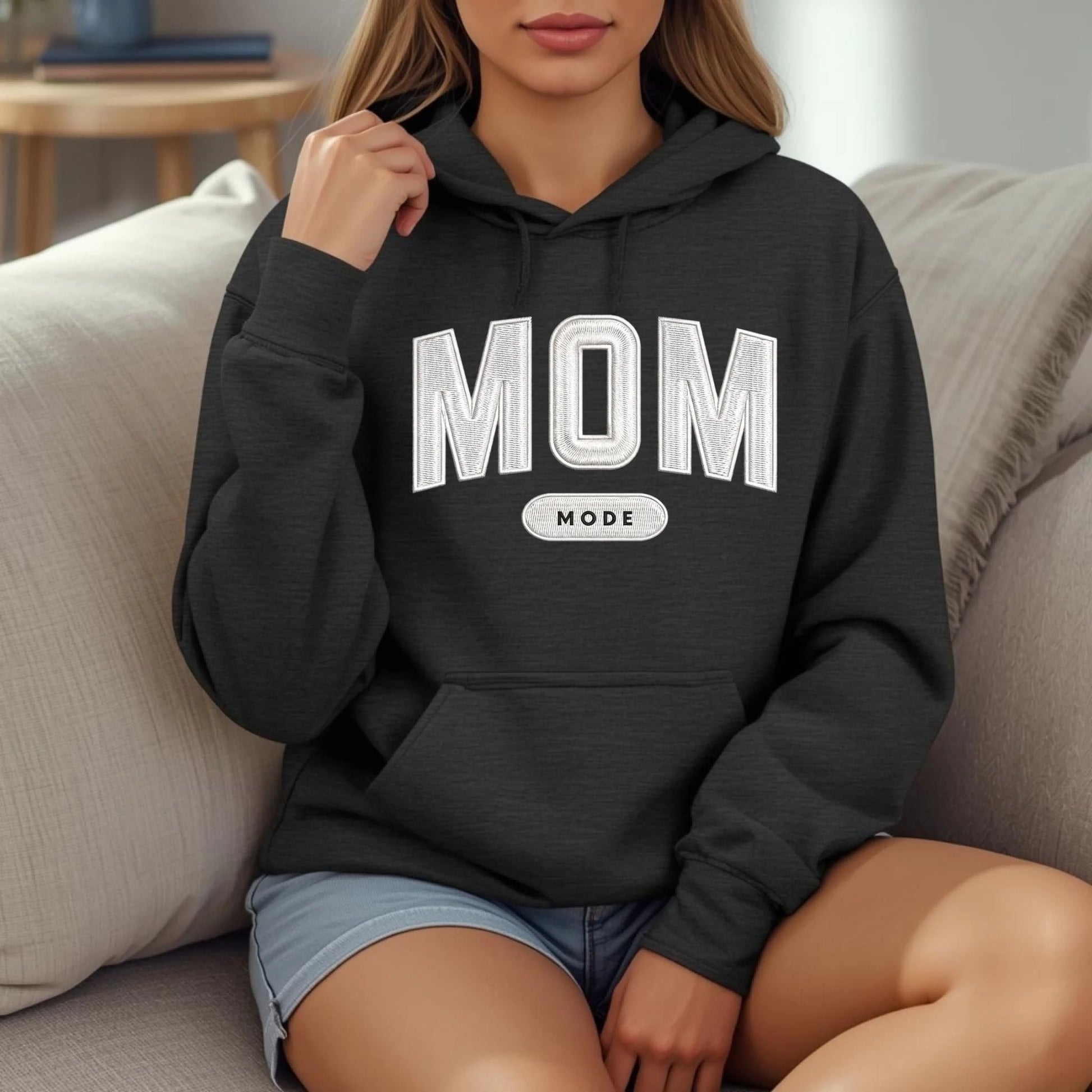 Person wearing a black hoodie with 'MOM MODE' text sitting on a couch.