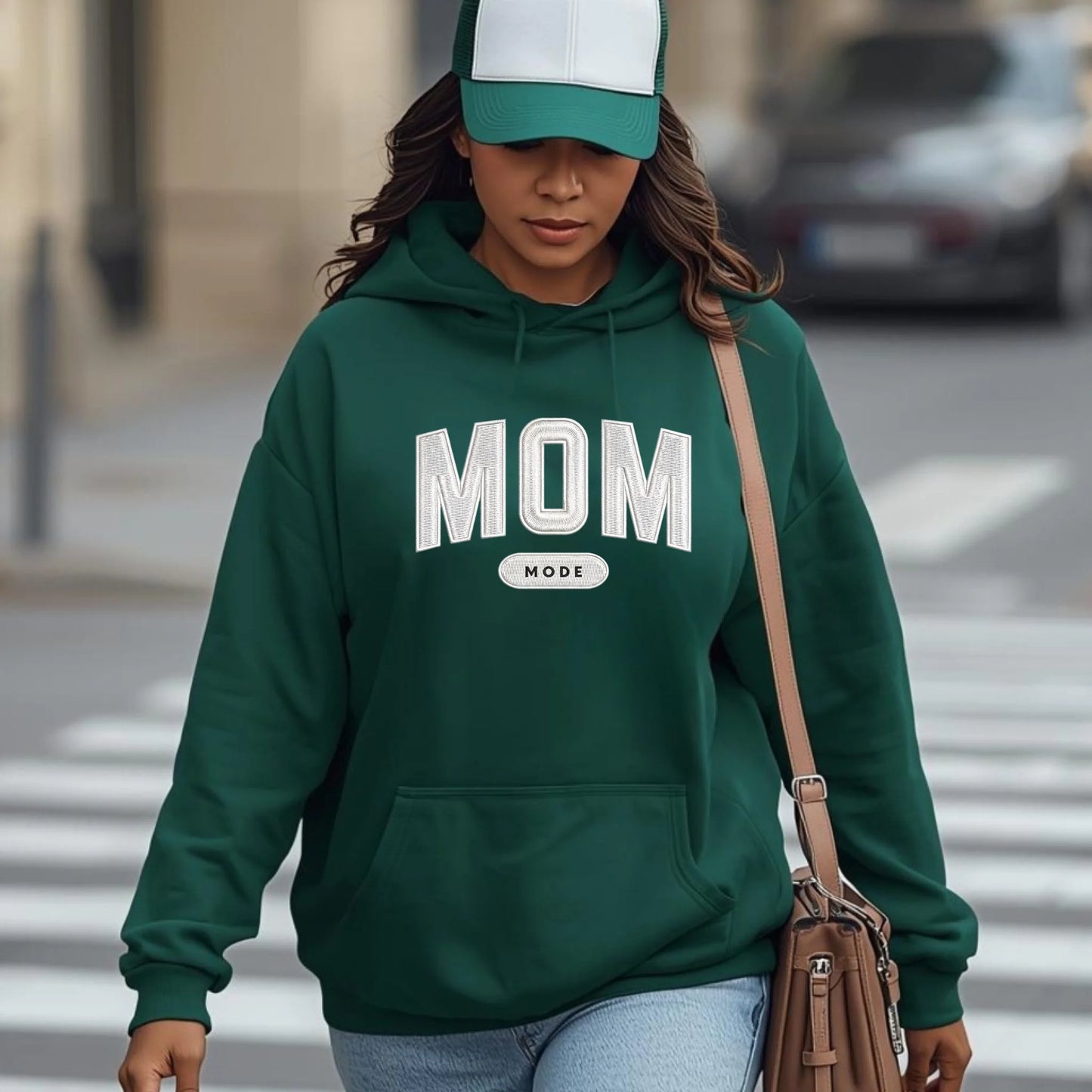 Woman wearing a forest green 'MOM' hoodie crossing a street.