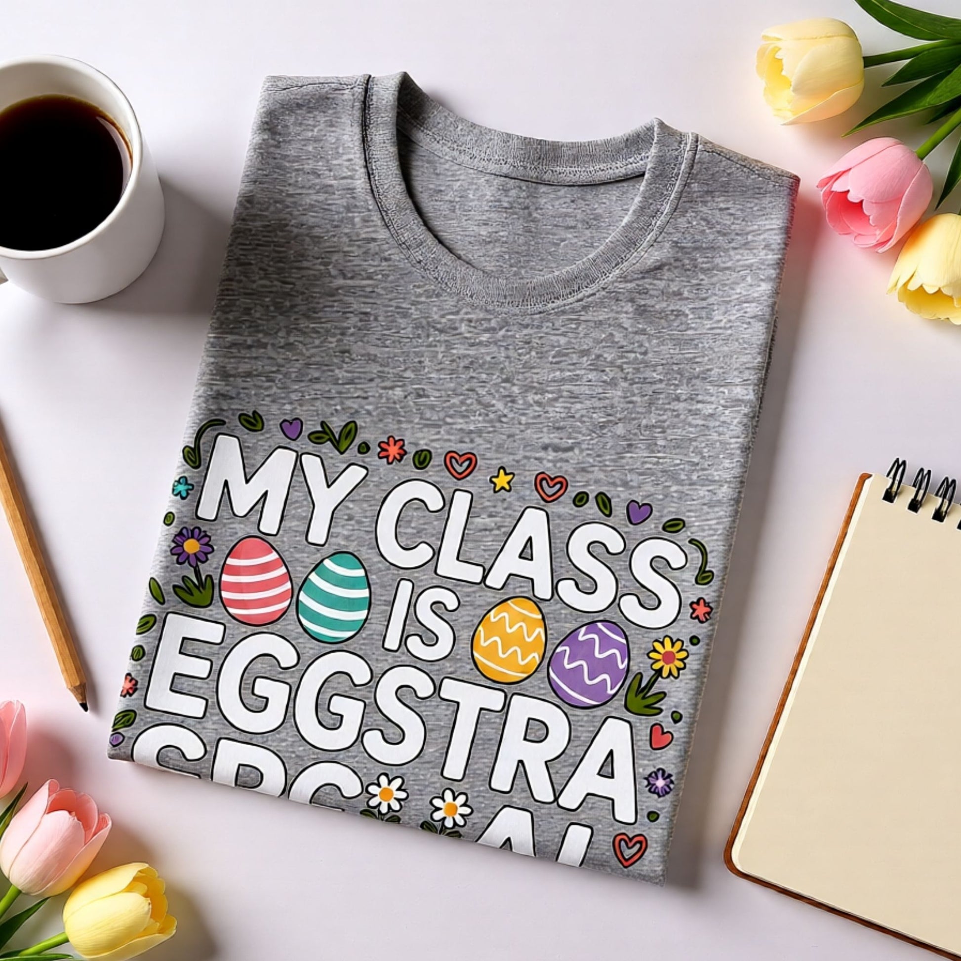 Gray t-shirt with Easter design on a white surface with coffee and flowers.