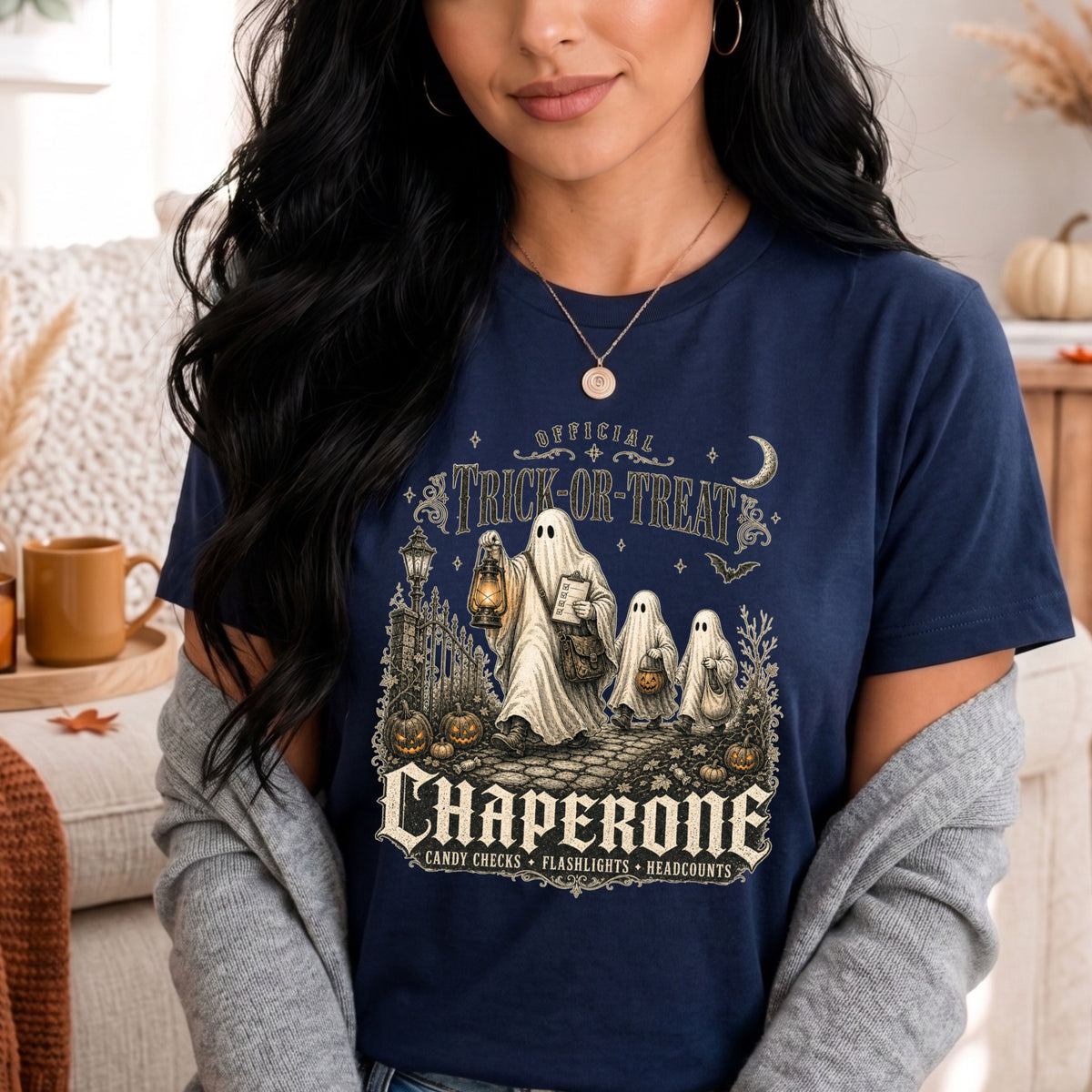 A woman wearing a navy blue graphic t-shirt with a Halloween-themed chaperone design, styled with a gray cardigan in a cozy indoor setting.
