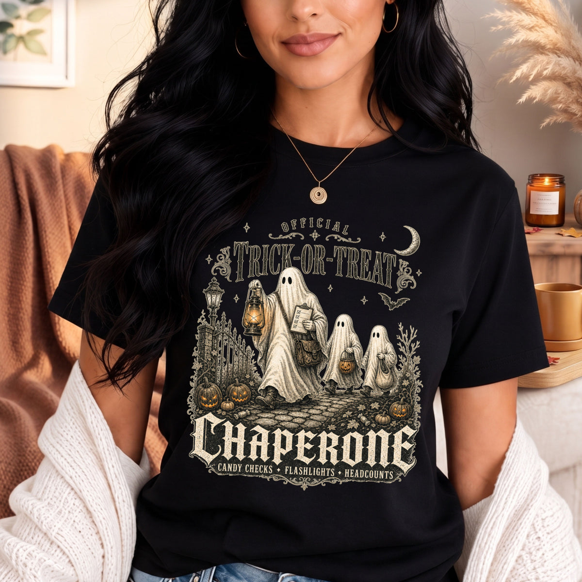 A woman wearing a black graphic t-shirt with a vintage-style Halloween design featuring ghosts, pumpkins, and the text 'Official Trick or Treat Chaperone'.