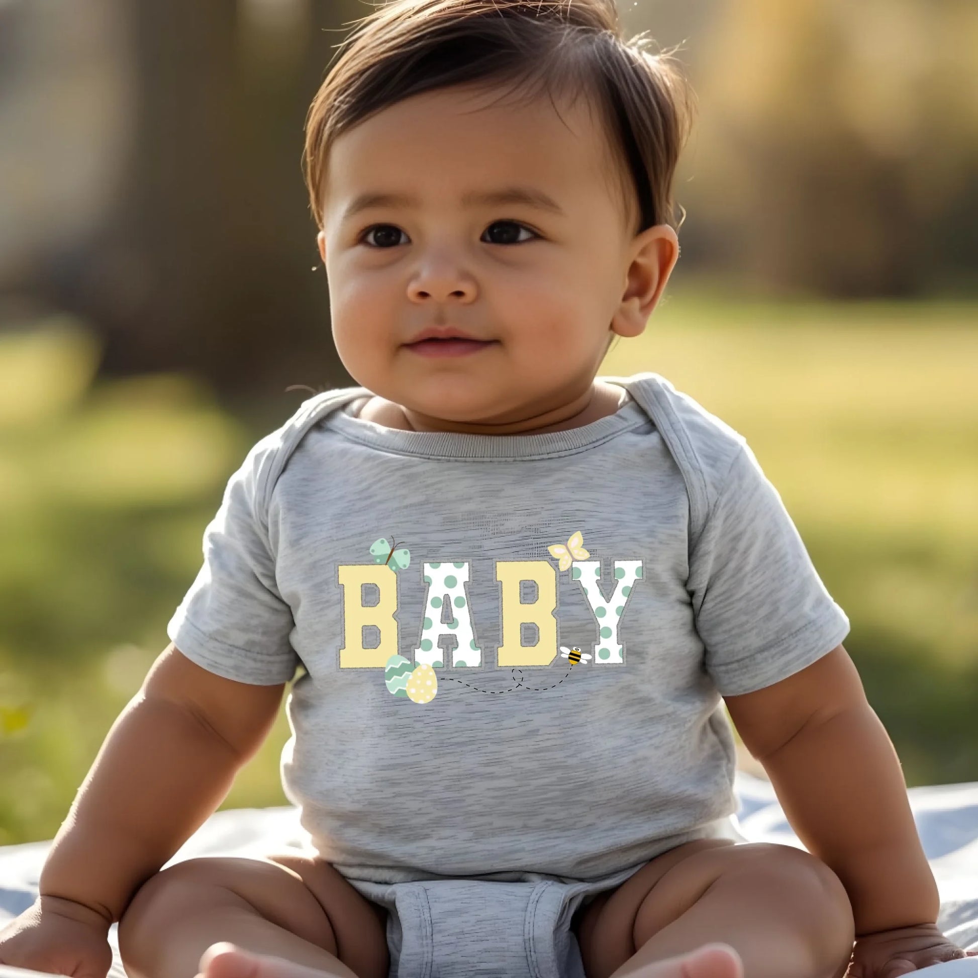 Baby wearing a heather gray “Baby” Easter t-shirt from a Mommy and Me matching collection, casual spring lifestyle photo.