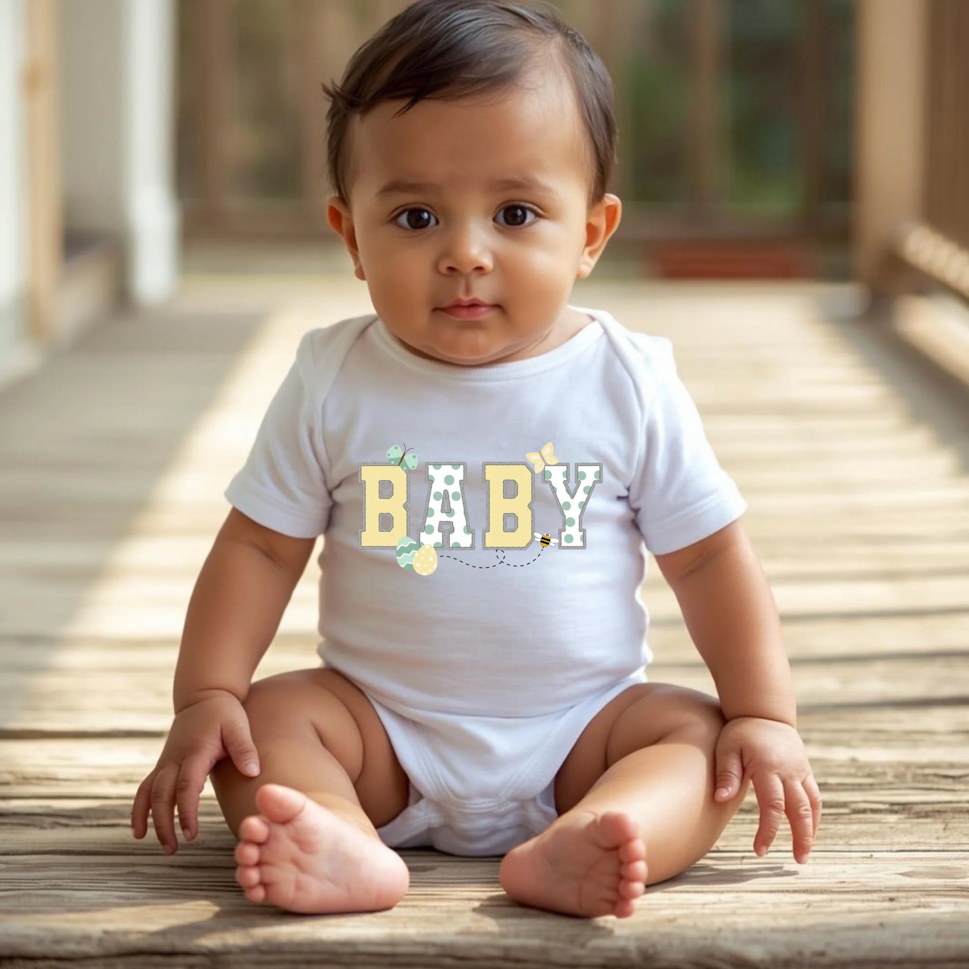 Baby wearing a white “Baby” Easter t-shirt from a Mommy and Me matching collection, seated outdoors in spring light.