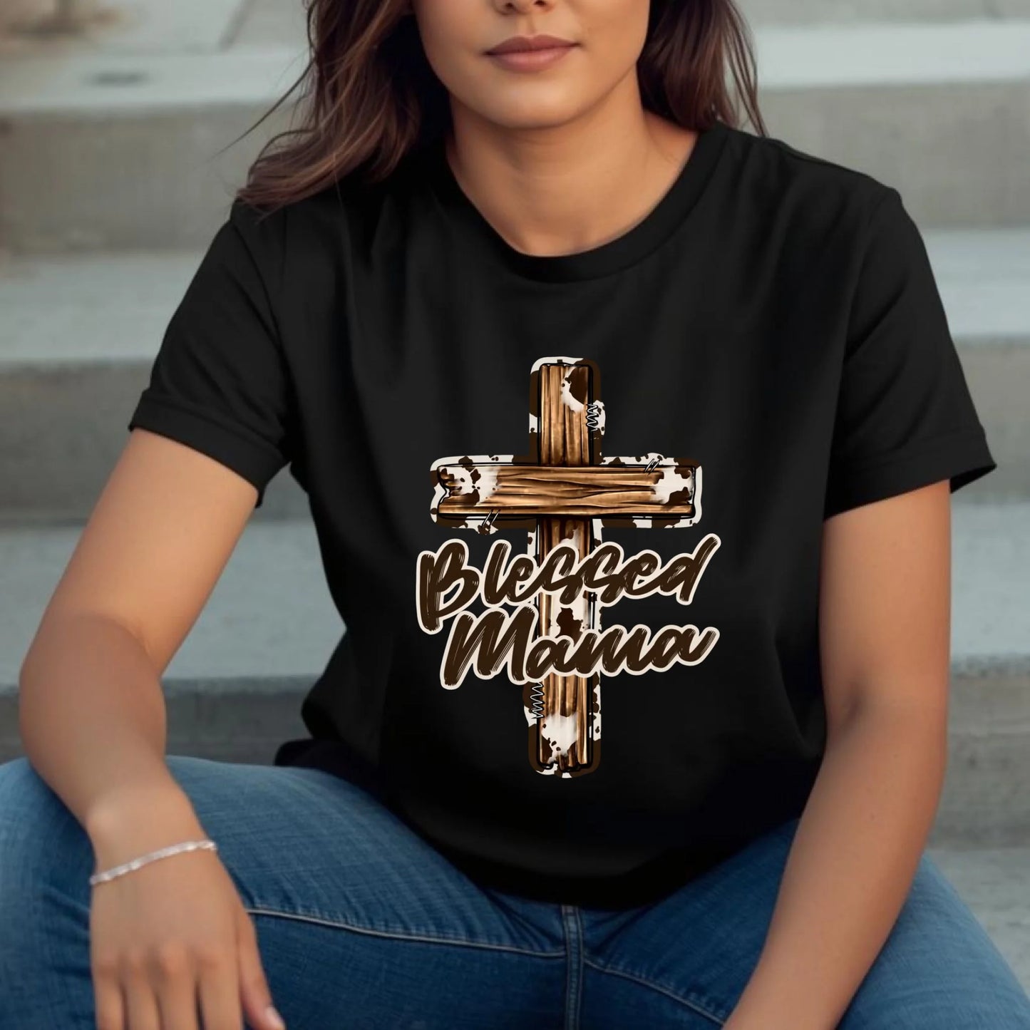 Woman wearing a black Blessed Mama cross t-shirt, relaxed seated pose with casual everyday styling.