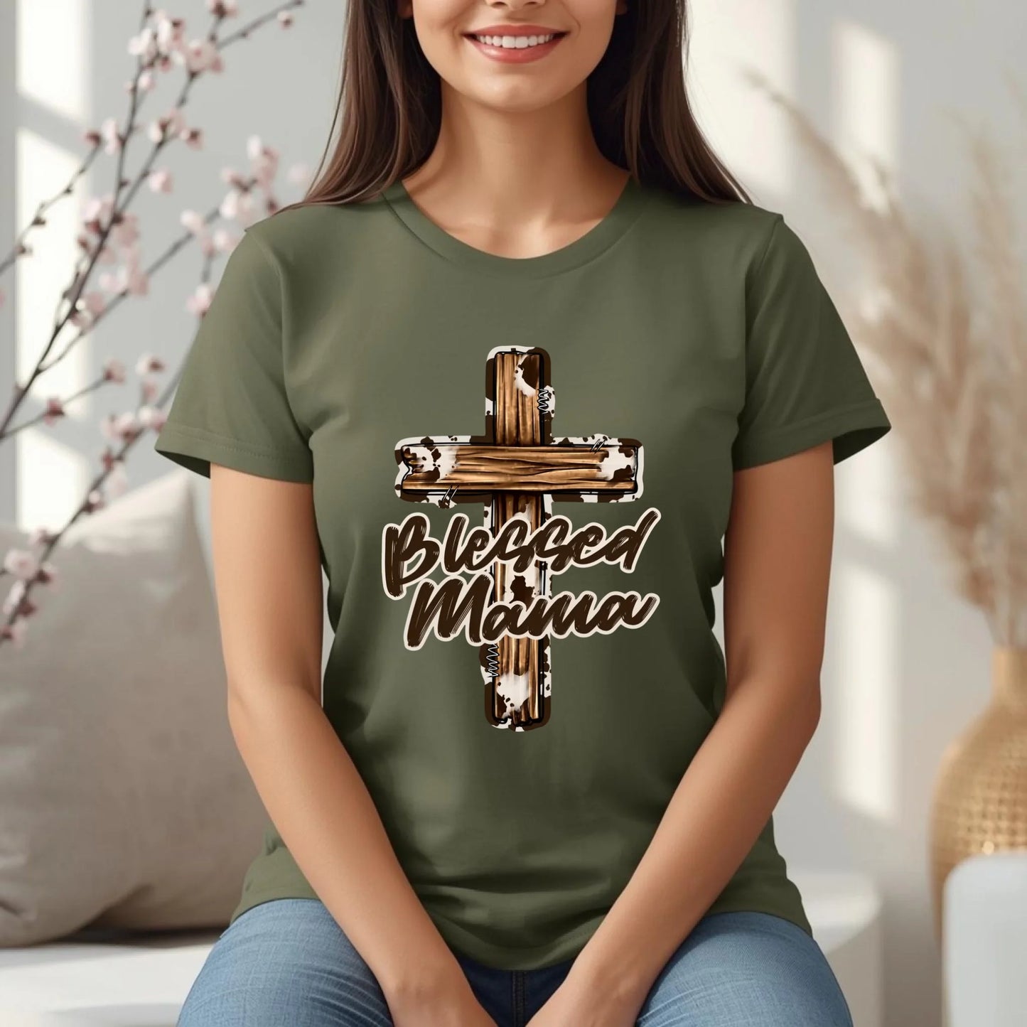 Woman wearing a Military  green Blessed Mama cross t-shirt, seated comfortably in a cozy lifestyle setting.
