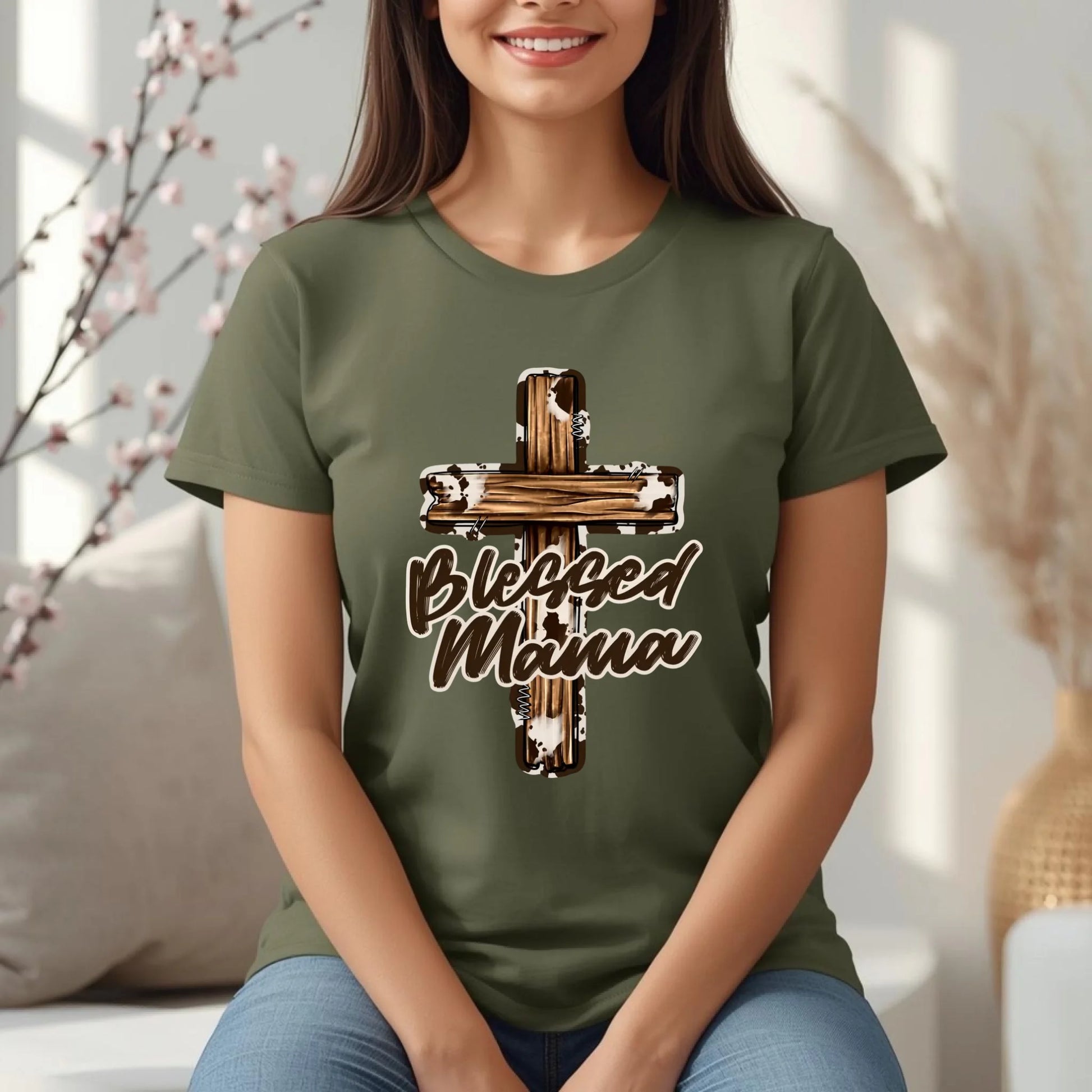 Woman wearing a Military  green Blessed Mama cross t-shirt, seated comfortably in a cozy lifestyle setting.
