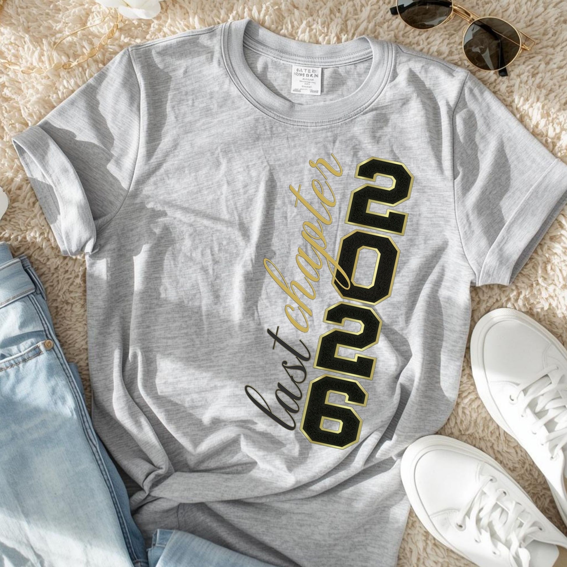 Gray t-shirt with '2026 Last Chapter' text on a beige surface with jeans and sneakers.