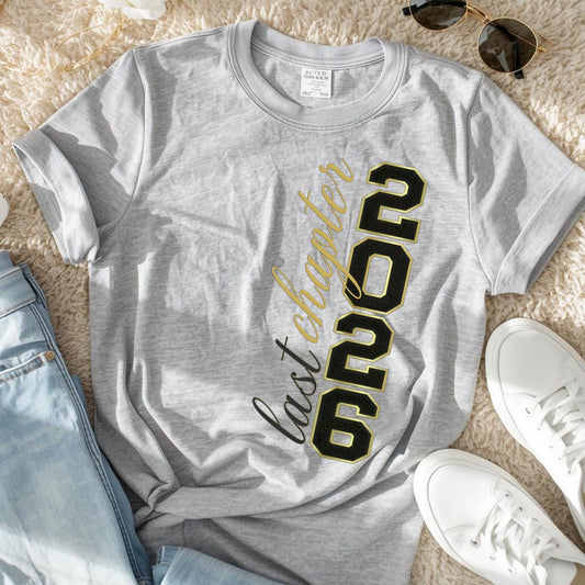 Gray t-shirt with '2026 Last Chapter' text on a beige surface with jeans and sneakers.