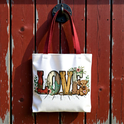 Rustic white tote bag with highland cow LOVE design hanging on weathered red barn wood.
