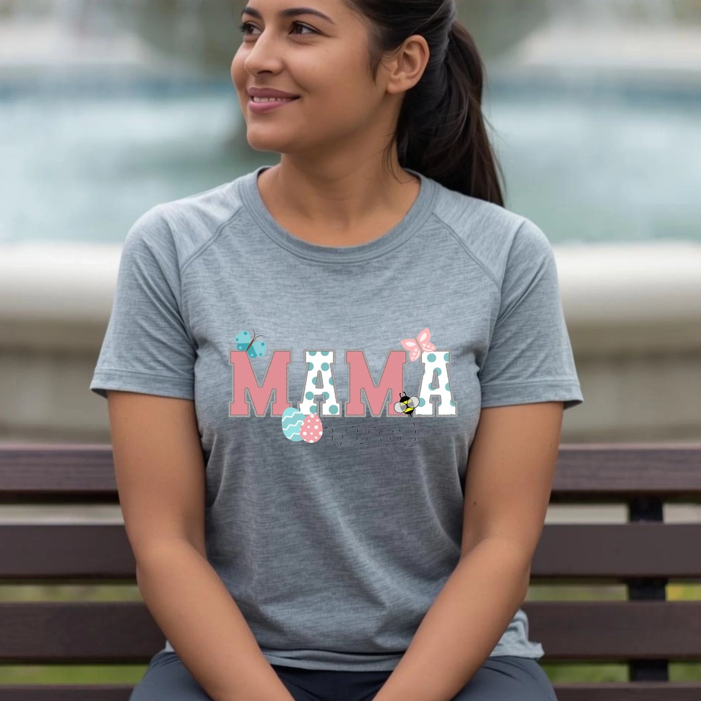 Woman sitting on a bench wearing a heather gray Bella Canvas “Mama” Easter t-shirt from a Mommy and Me matching collection.