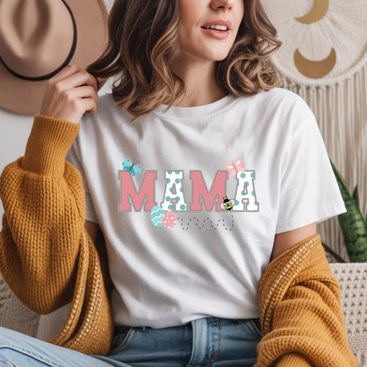 Woman wearing a white Bella Canvas Mommy and Me “Mama” Easter t-shirt with pastel spring graphics, casual indoor lifestyle photo.
