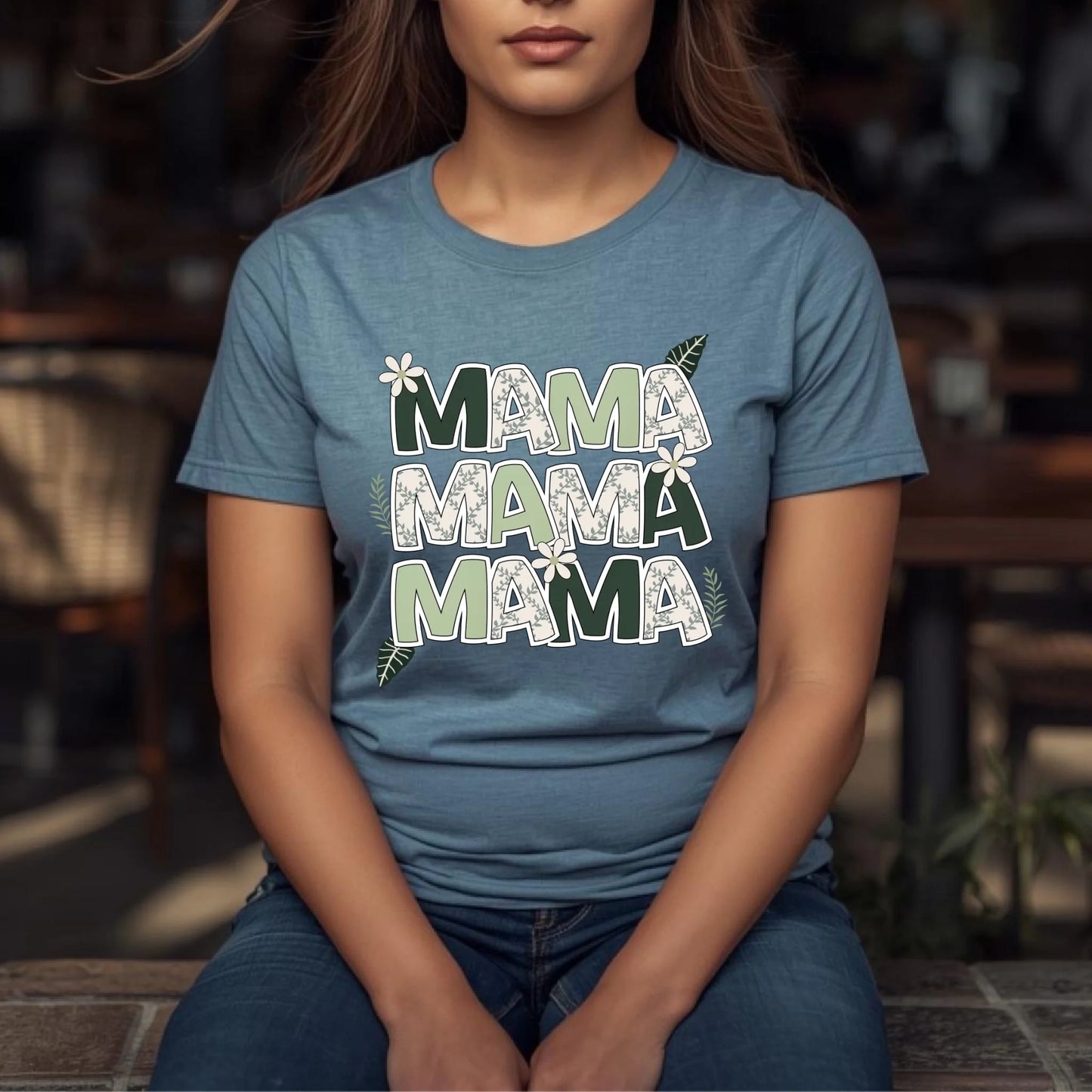 Woman seated outdoors wearing a blue floral “Mama” shirt styled for a relaxed everyday look.