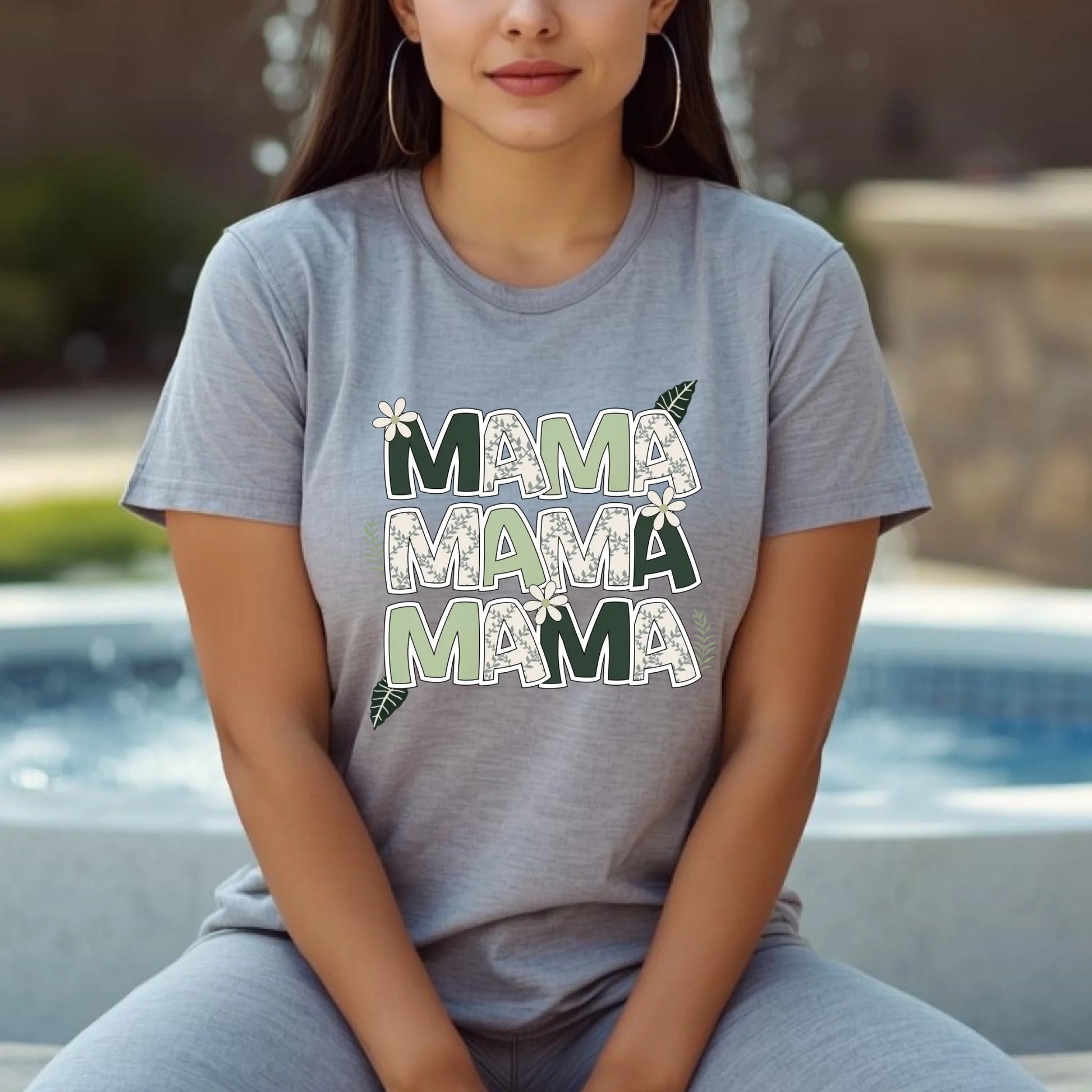 Woman sitting comfortably wearing a gray Bella Canvas “Mama” floral letter t-shirt in natural daylight.