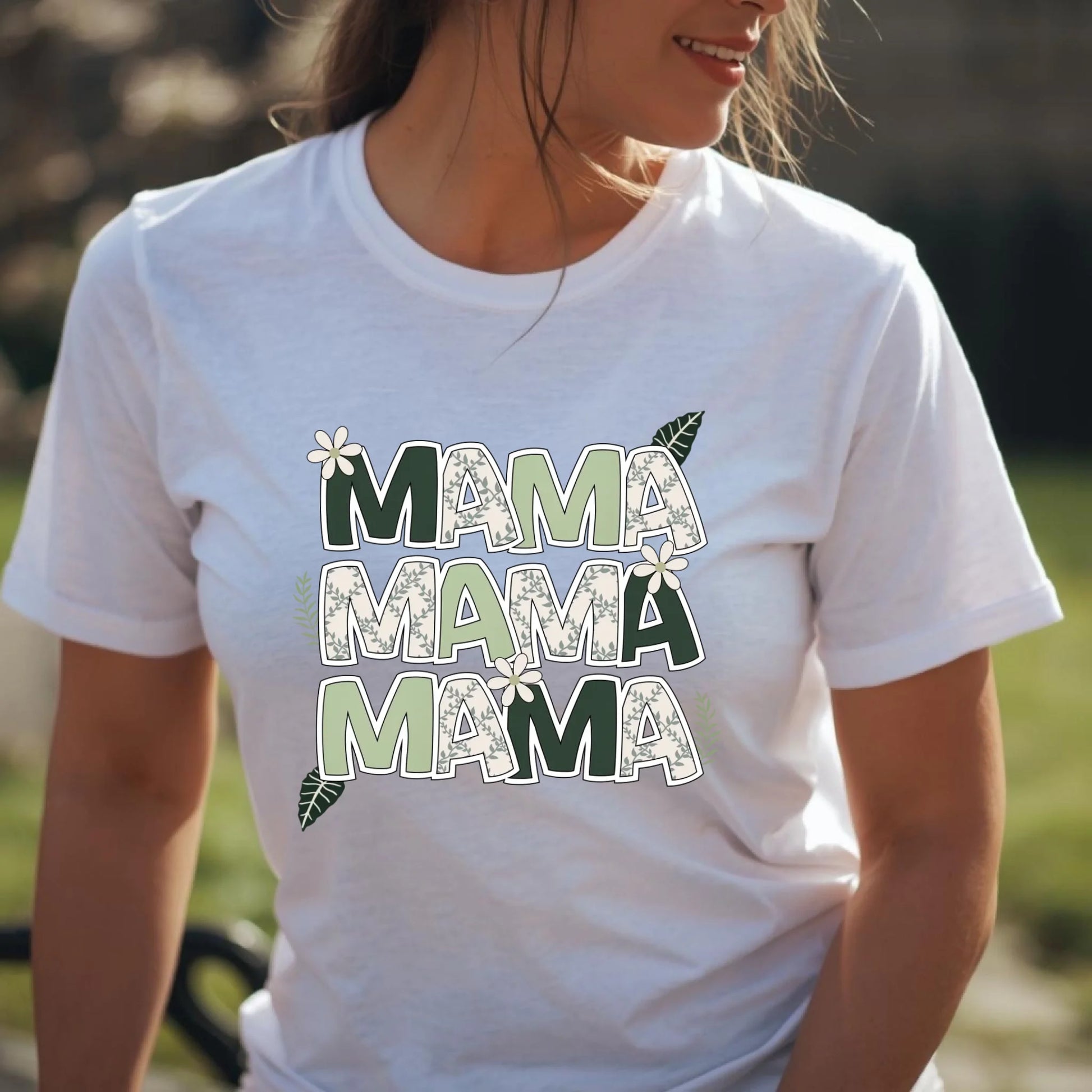 Close-up of a woman wearing a white Bella Canvas t-shirt featuring a floral “Mama” letter design in sage and botanical tones.