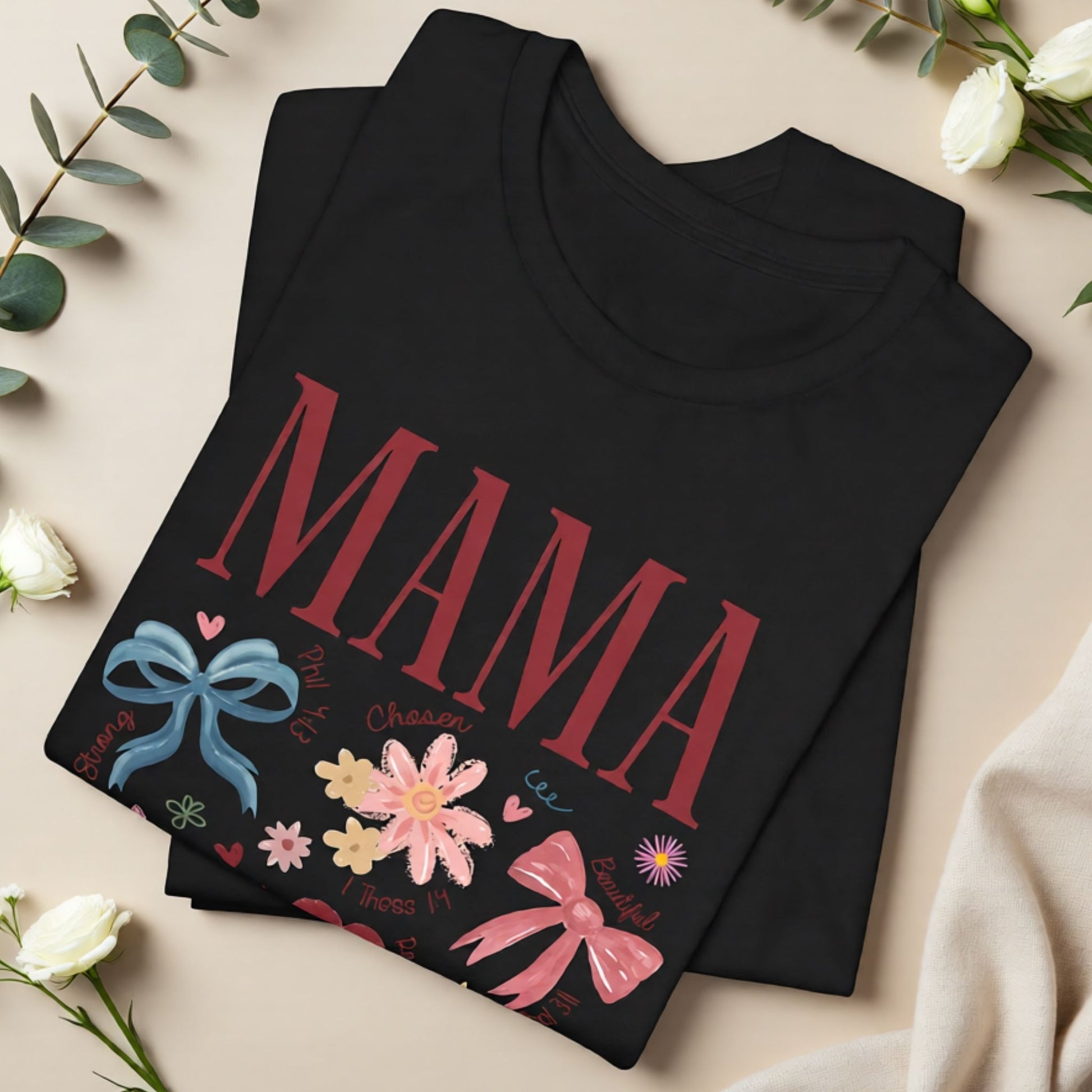 Flat lay of a black Mama floral t-shirt with decorative bows, flowers, and uplifting scripture-inspired elements for Mother’s Day.