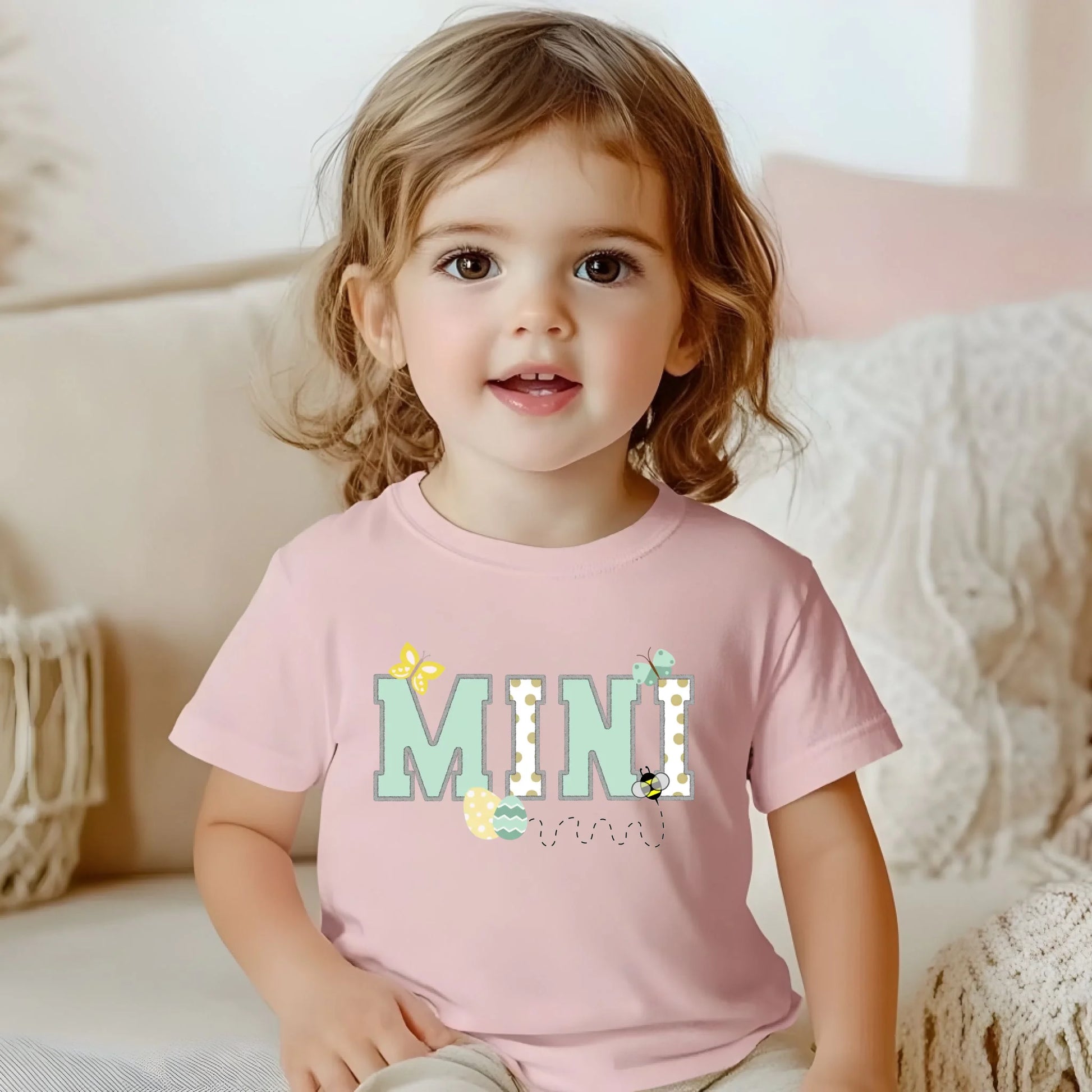 Toddler wearing a pink “Mini” Easter t-shirt from a Mommy and Me matching set, photographed indoors in soft natural light.