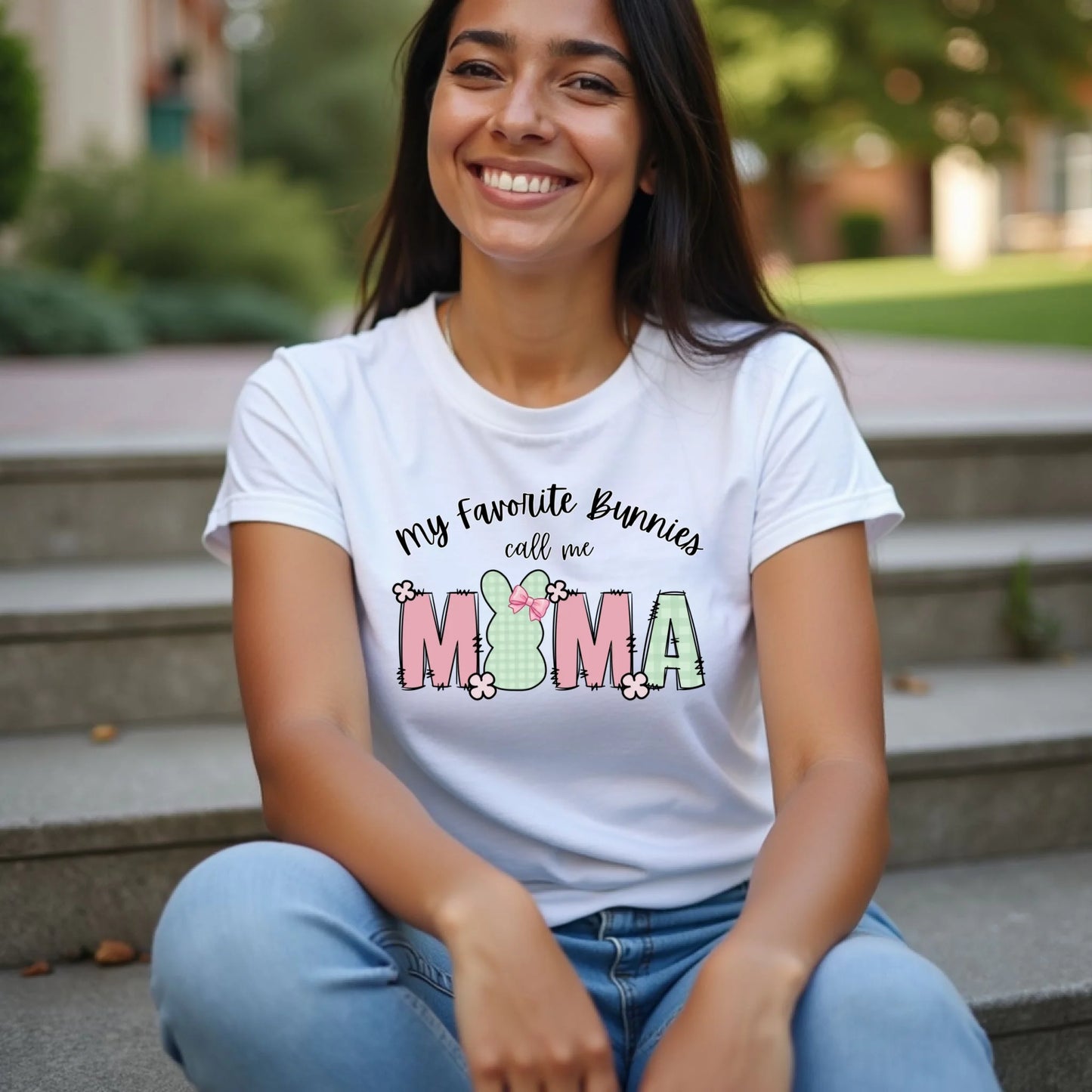 Woman sitting on steps wearing a white Bella Canvas t-shirt with a “My Favorite Bunnies Call Me Mama” Easter bunny design in soft pastel colors.