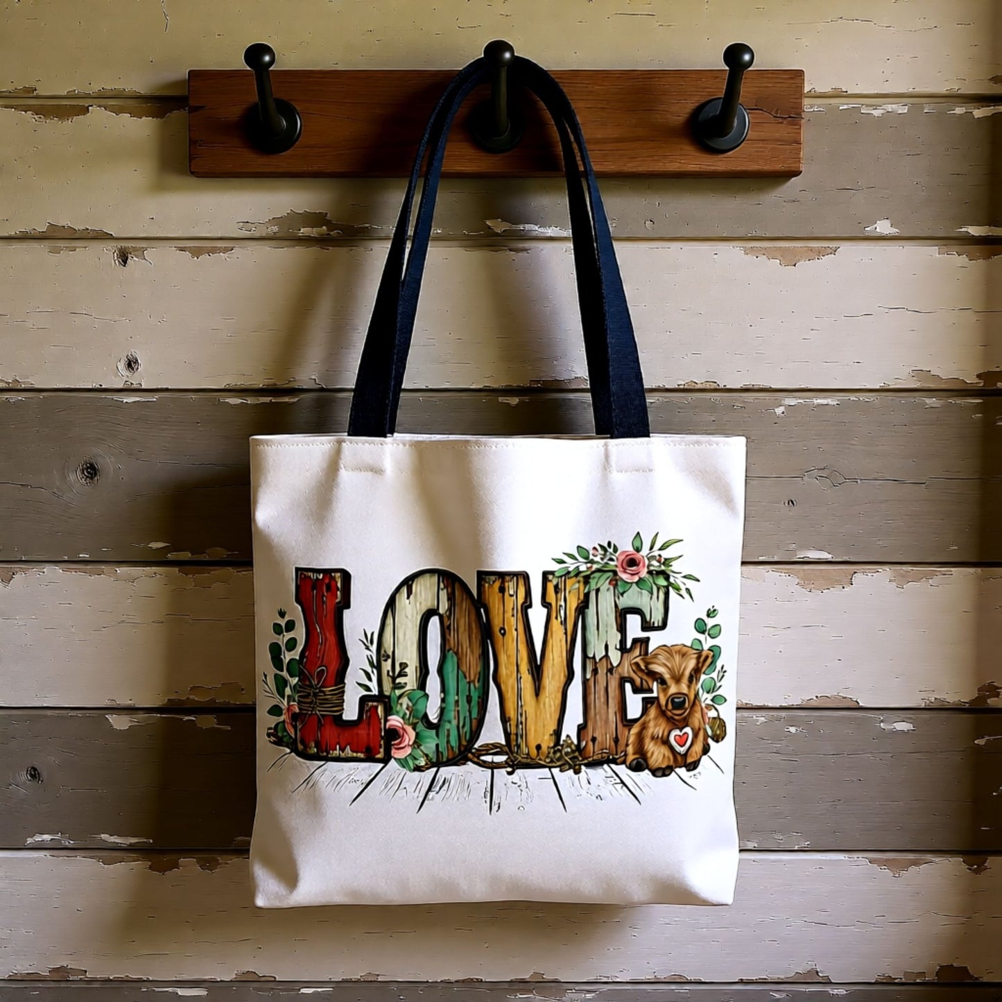 Tote bag with 'LOVE' and teddy bear design hanging on a wooden wall hook.
