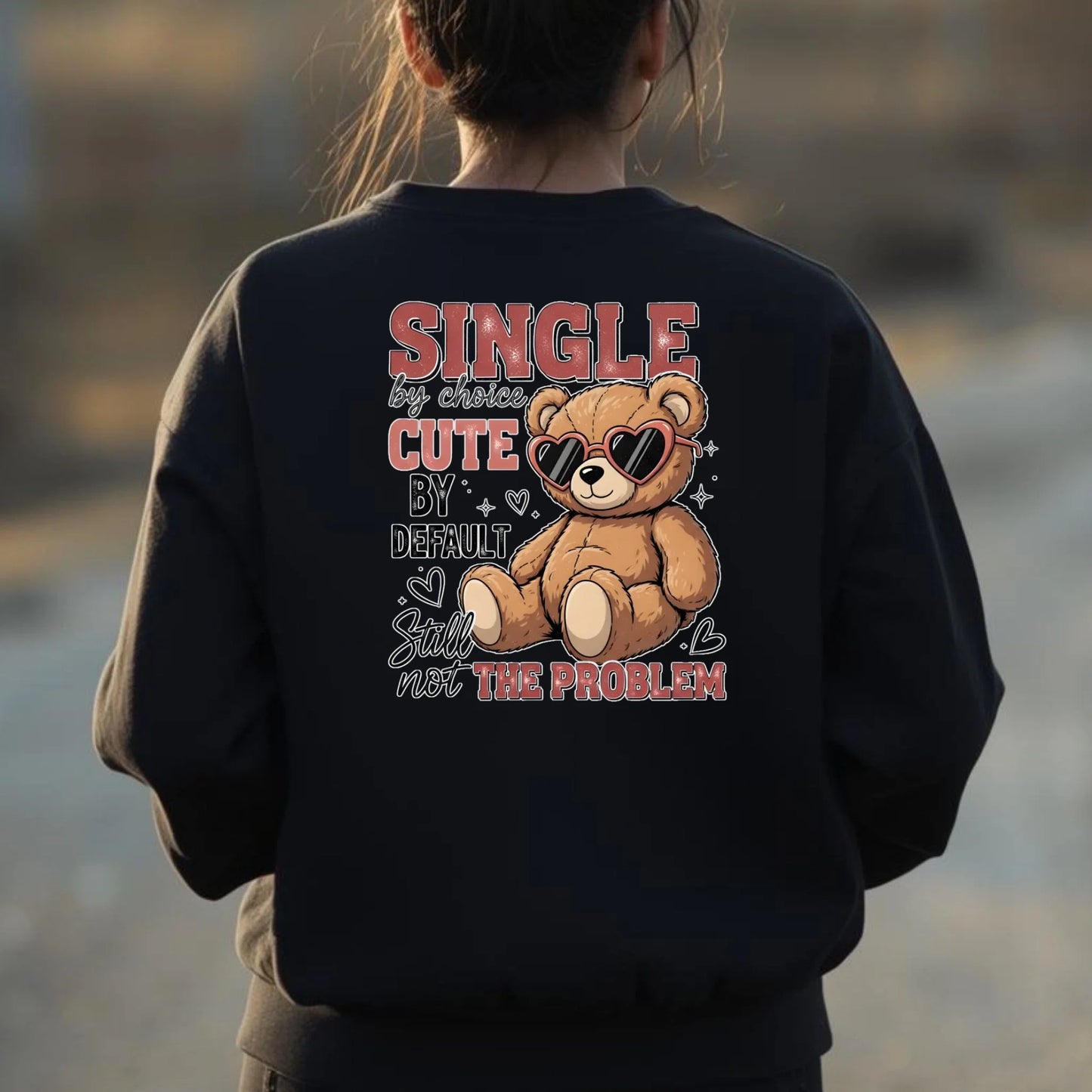 Person wearing a black sweatshirt with a teddy bear graphic and text at a beach.