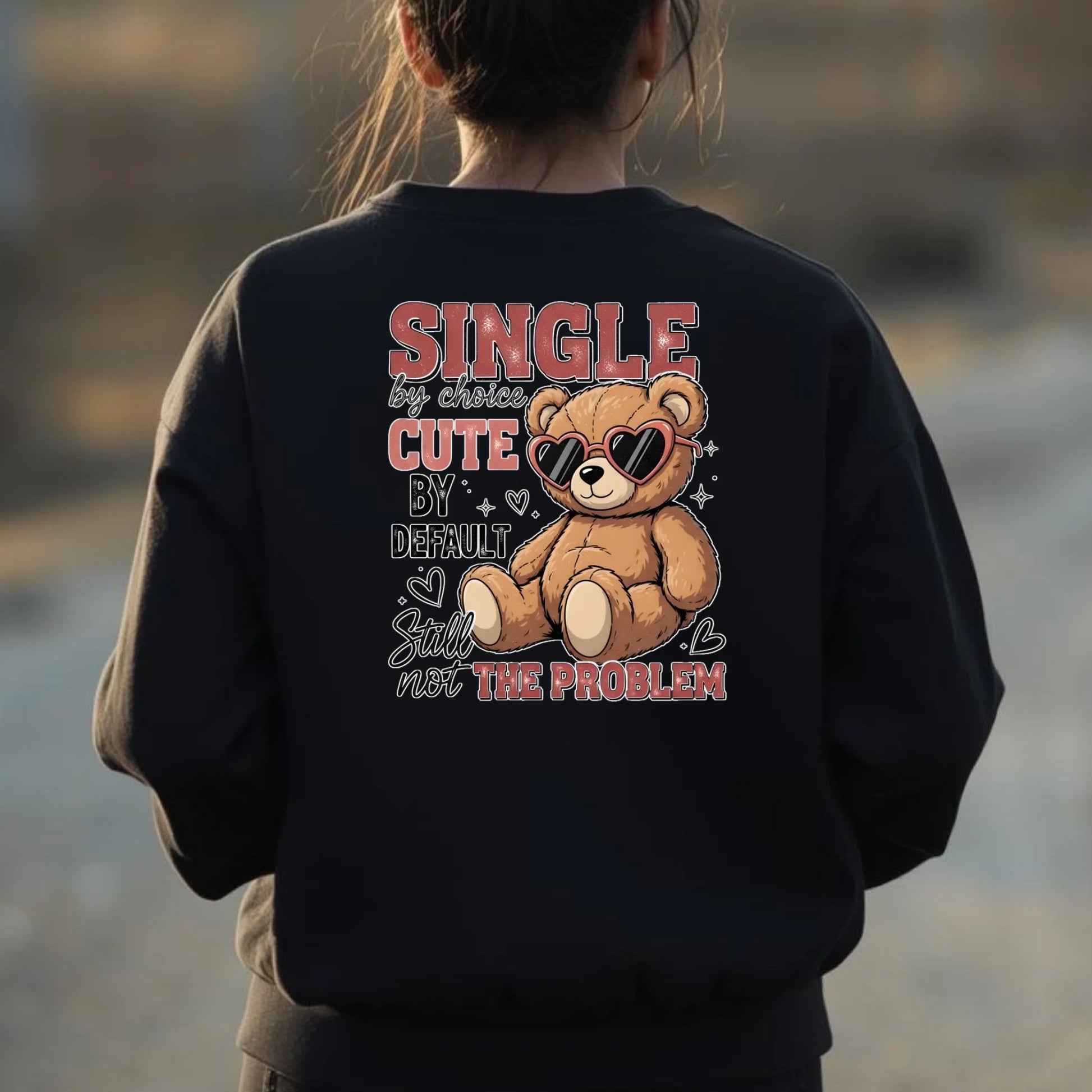Person wearing a black sweatshirt with a teddy bear graphic and text at a beach.