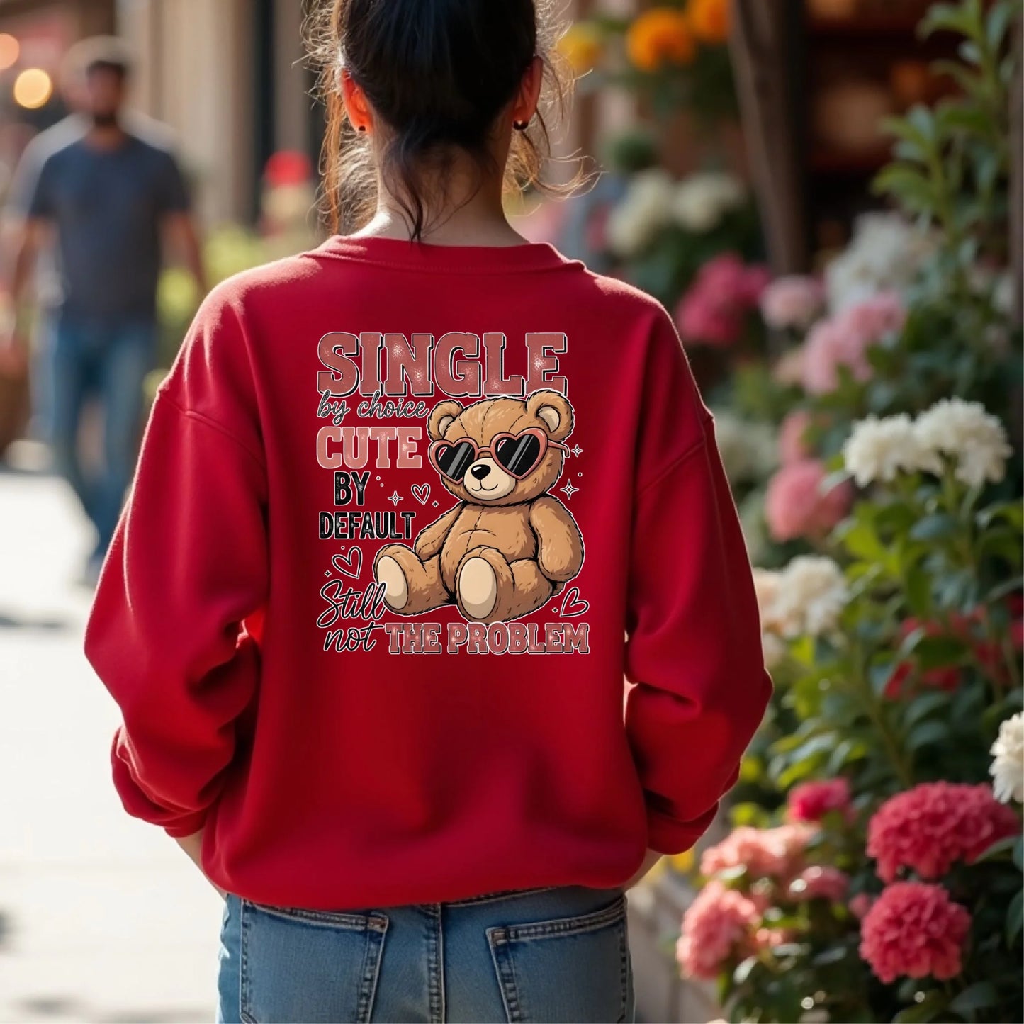 Person wearing a red sweatshirt with a teddy bear graphic and text in an urban setting with flowers.