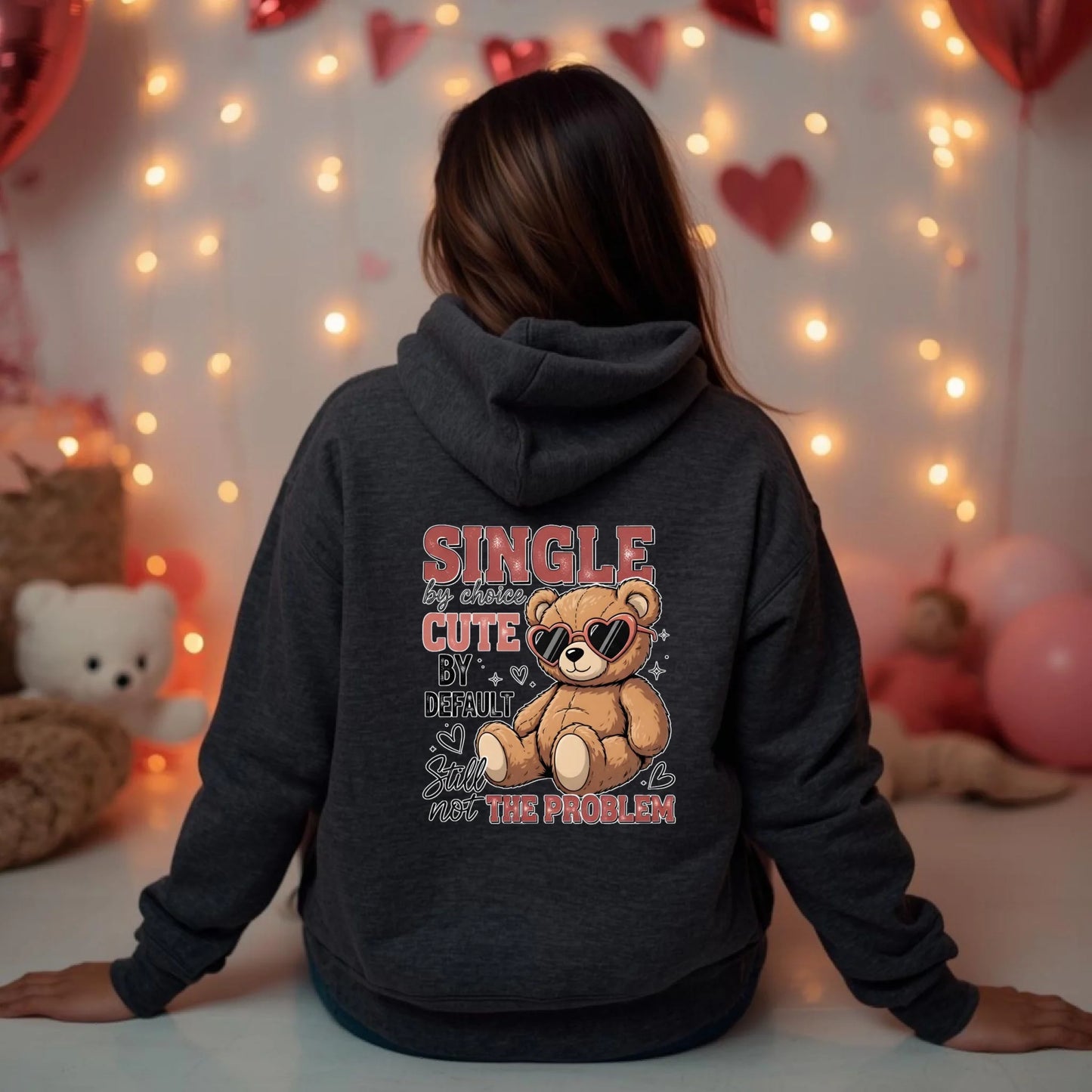 Person wearing a hoodie with a teddy bear graphic and text in a room decorated with lights and balloons.