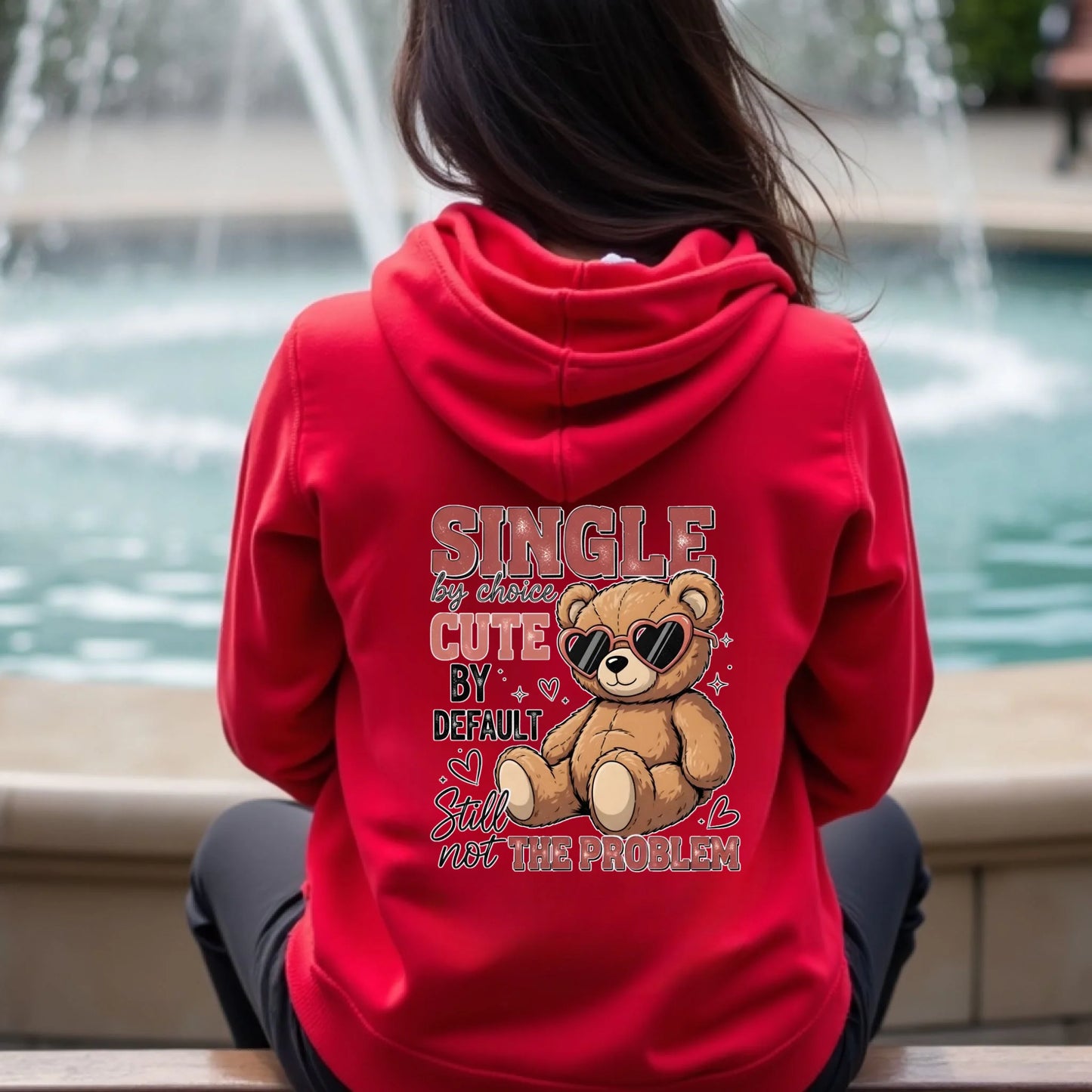 Person wearing a red hoodie with a teddy bear graphic and text in an outdoor setting.