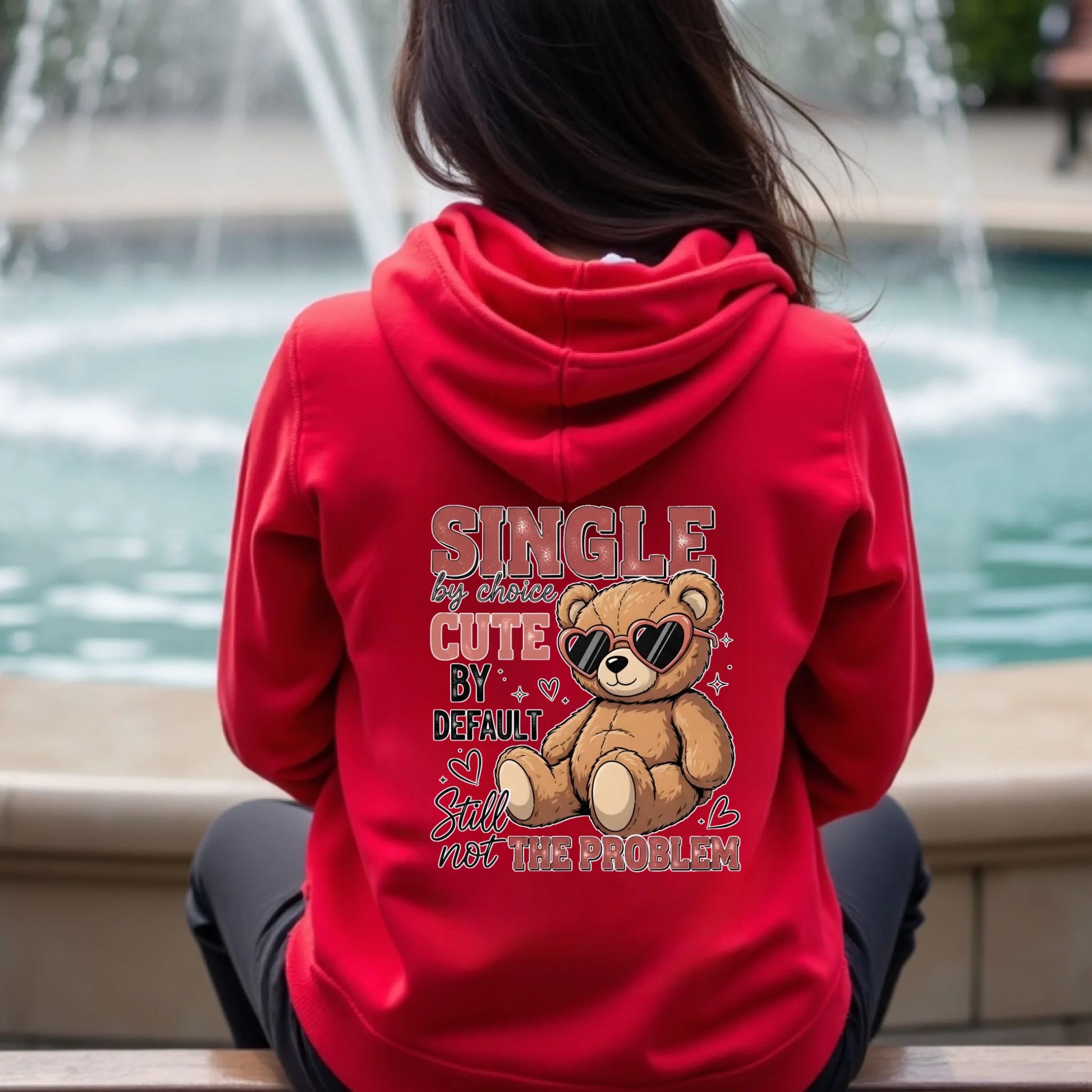 Person wearing a red hoodie with a teddy bear graphic and text in an outdoor setting.