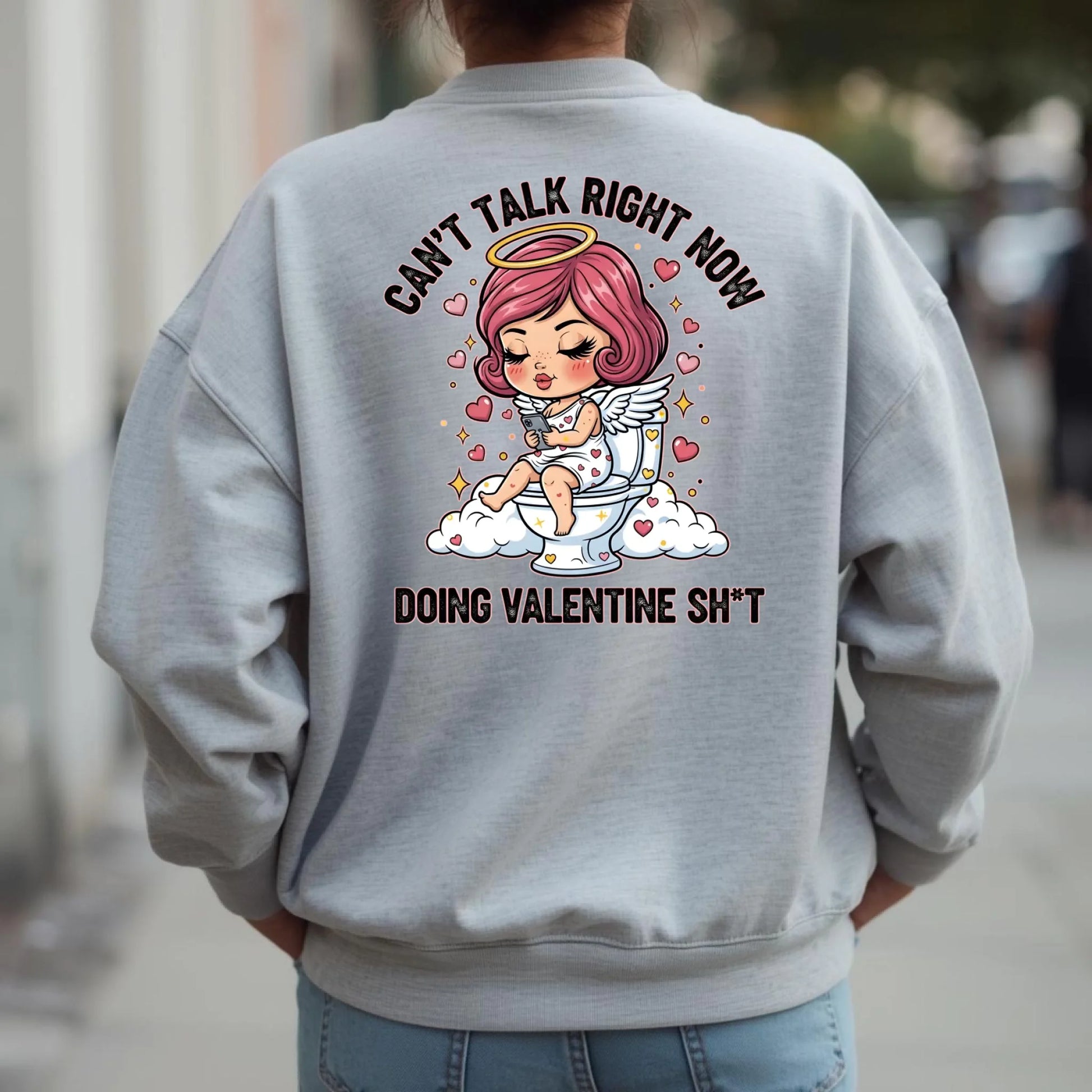 Person wearing a Ash crewneck sweatshirt with a graphic design on the back, featuring a humorous Toilet Cupid Valentine graphic.