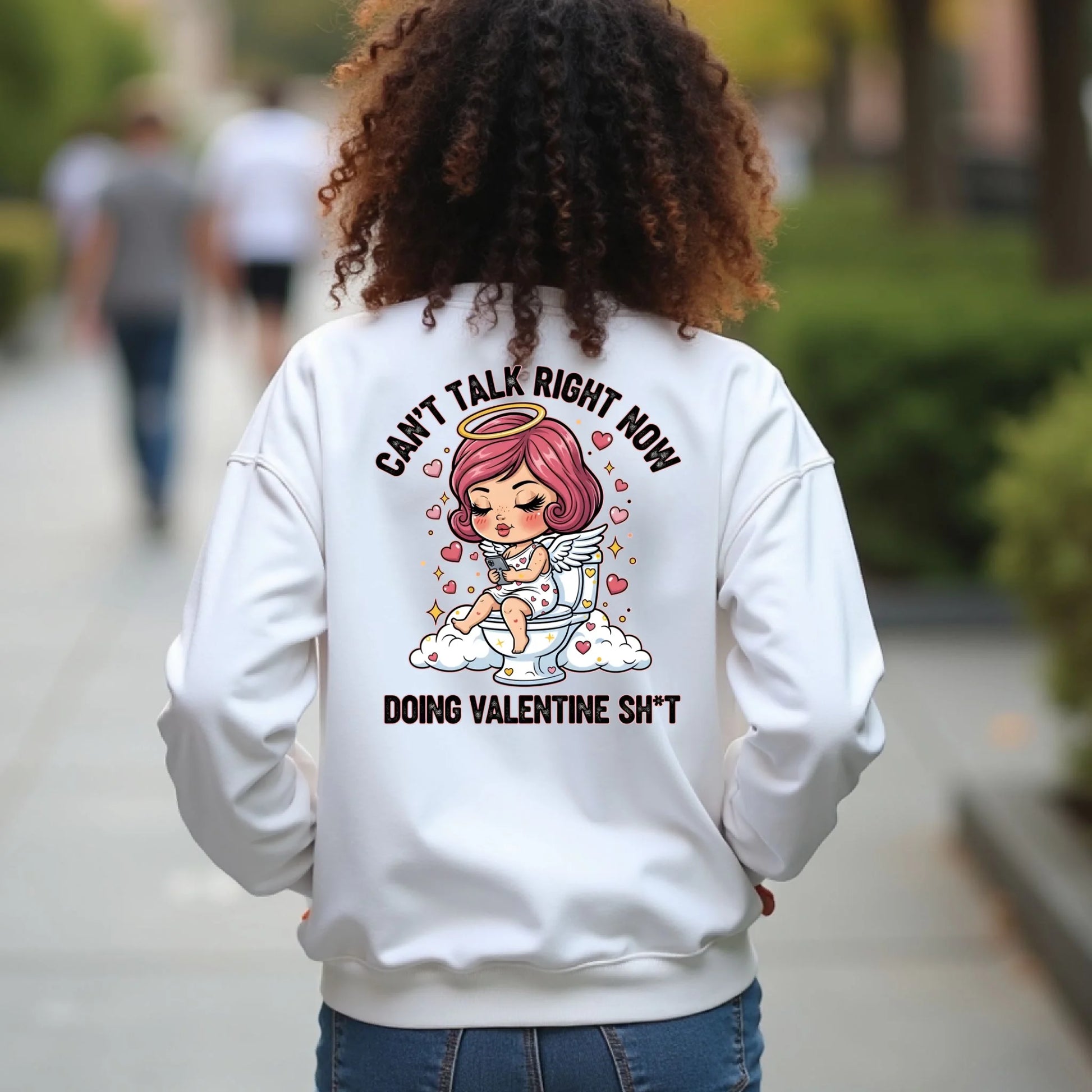Person wearing a White crewneck sweatshirt with a graphic design on the back, featuring a humorous Toilet Cupid Valentine graphic.