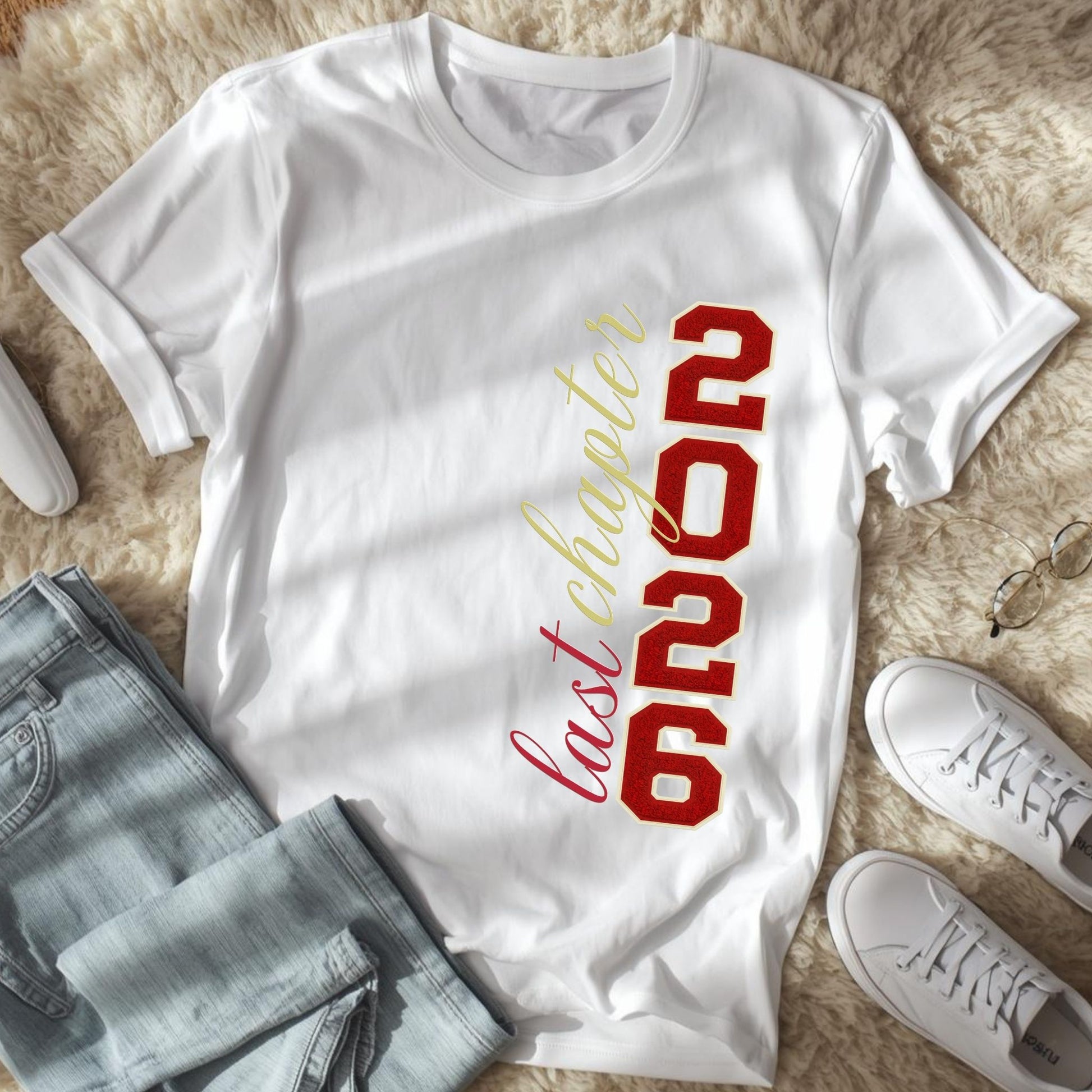 White t-shirt with '2026 last chapter' text on a fluffy surface with jeans and shoes.